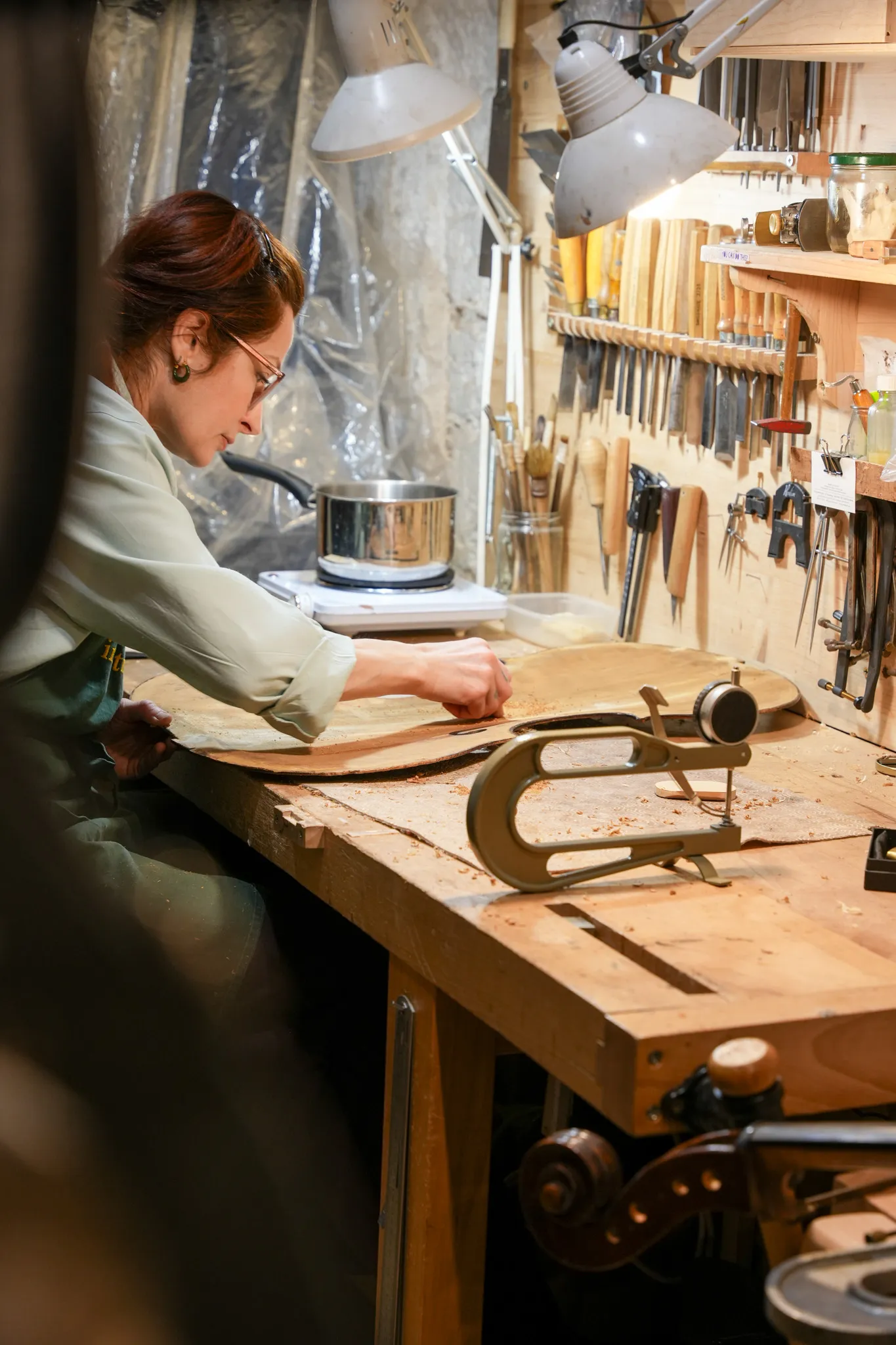 Une femme travaillant sur une pièce de bois dans un atelier d'ébénisterie bien équipé avec des outils accrochés au mur.