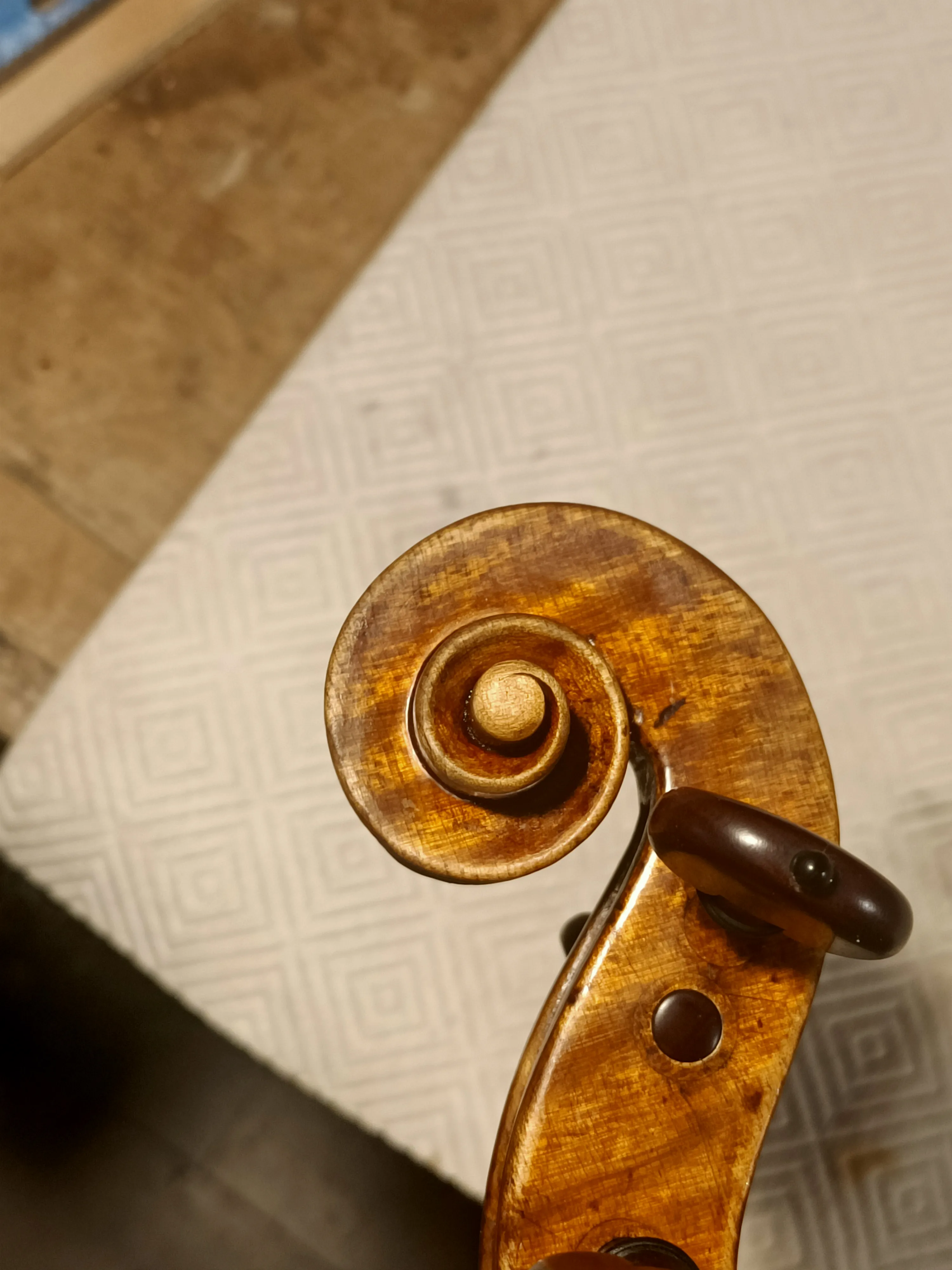 Gros plan sur la volute brun doré d'un violon avec une table en papier texturé en arrière-plan.