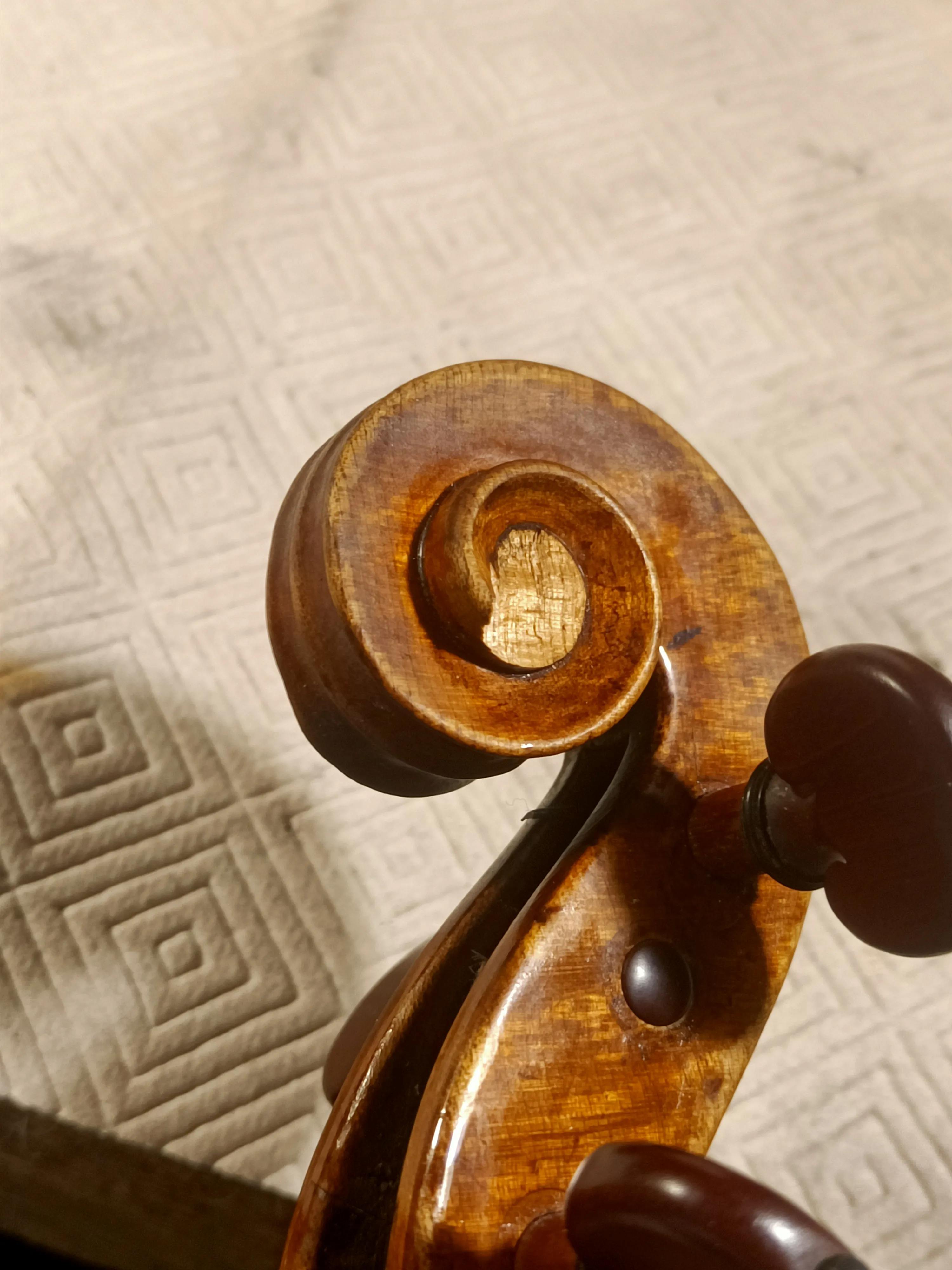 Gros plan sur la volute en bois sculpté d'un violon posé sur une surface claire avec un motif géométrique.