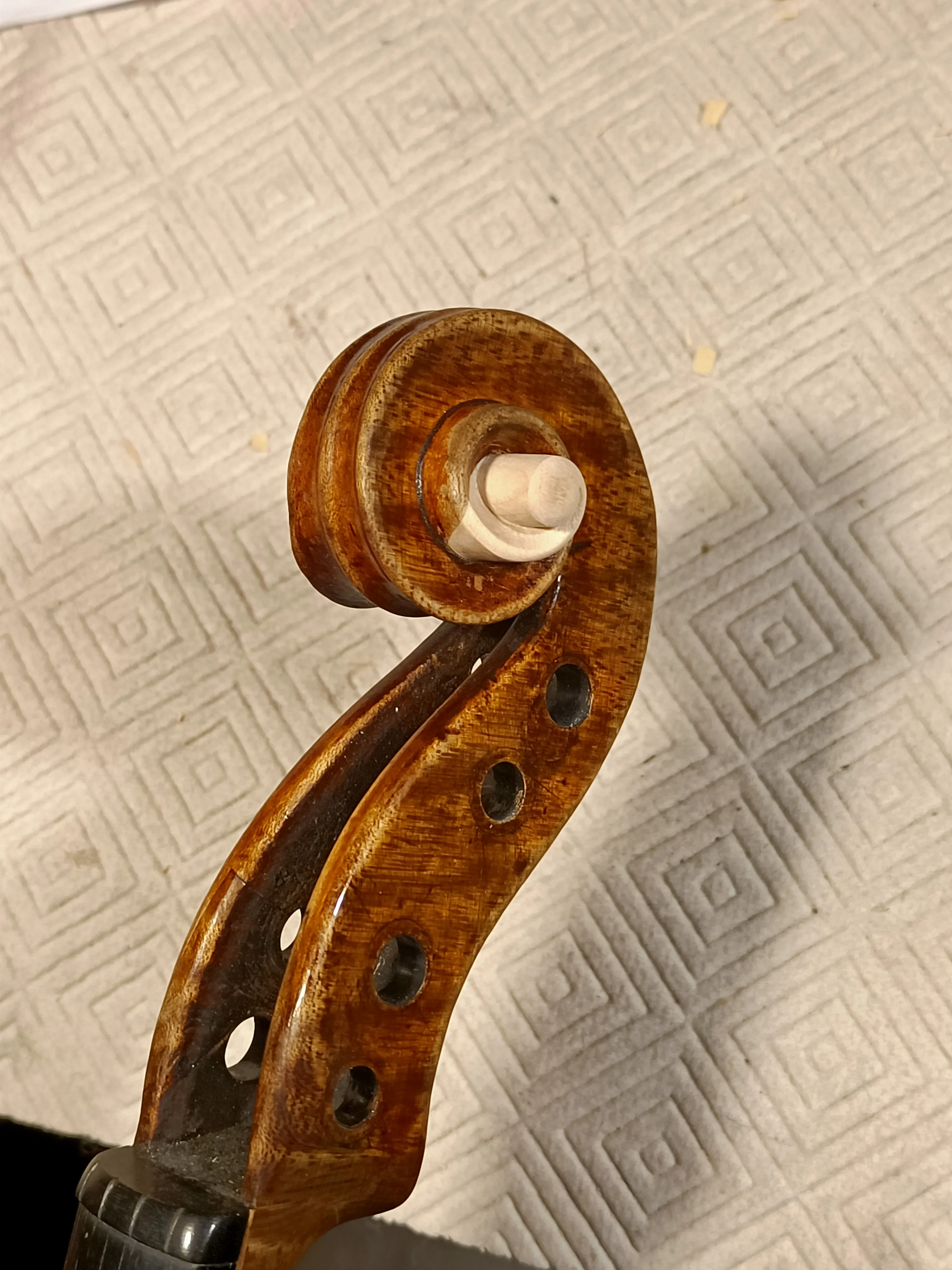 Gros plan sur le rouleau en bois verni d'un violon posé sur un tissu à motif géométrique.