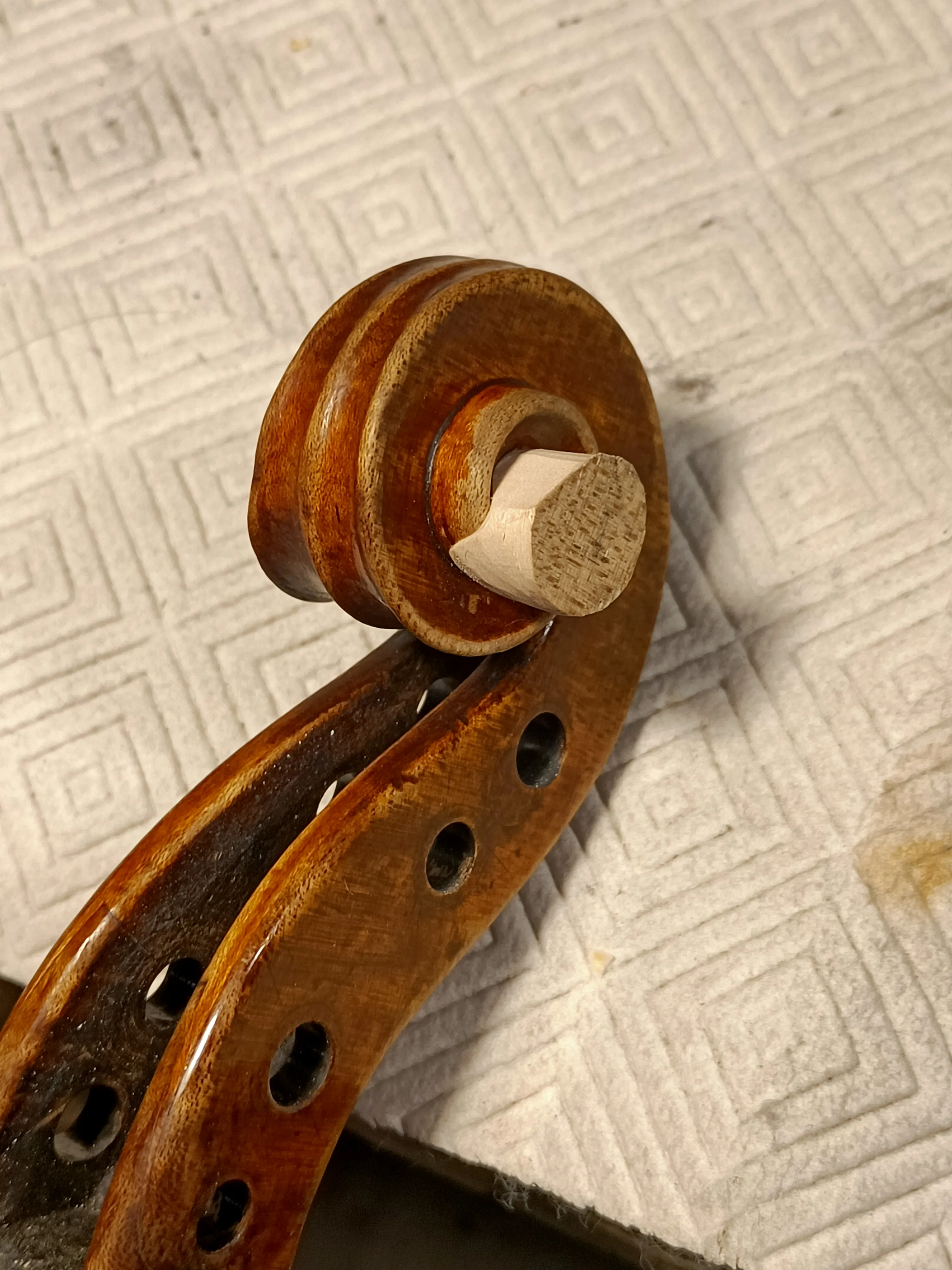 Volute et pique d'un violon en bois sur un tissu blanc à motifs géométriques.