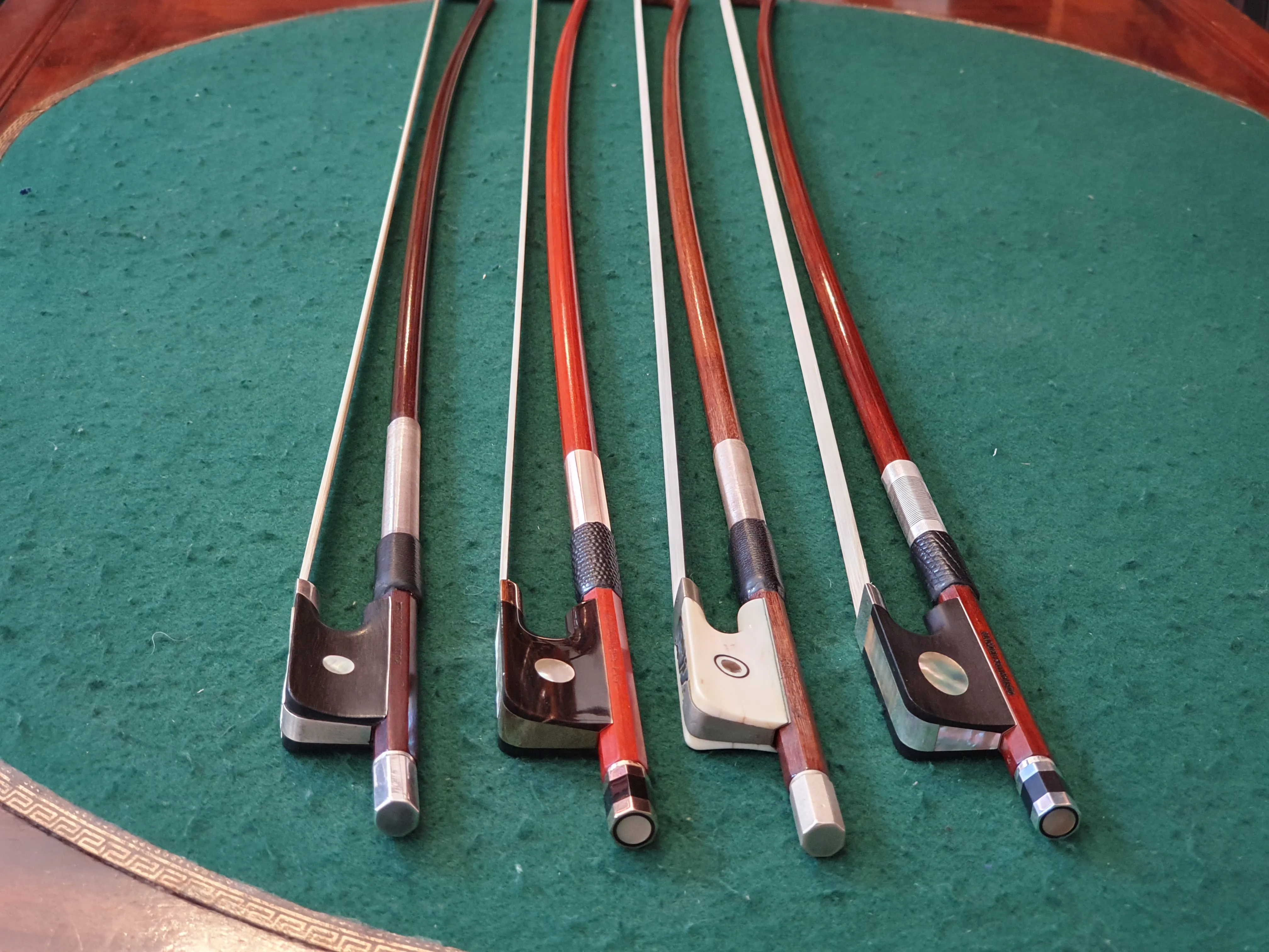 Quatre archets de violon alignés sur un tissu vert avec des tibias en bois rouge et brun.