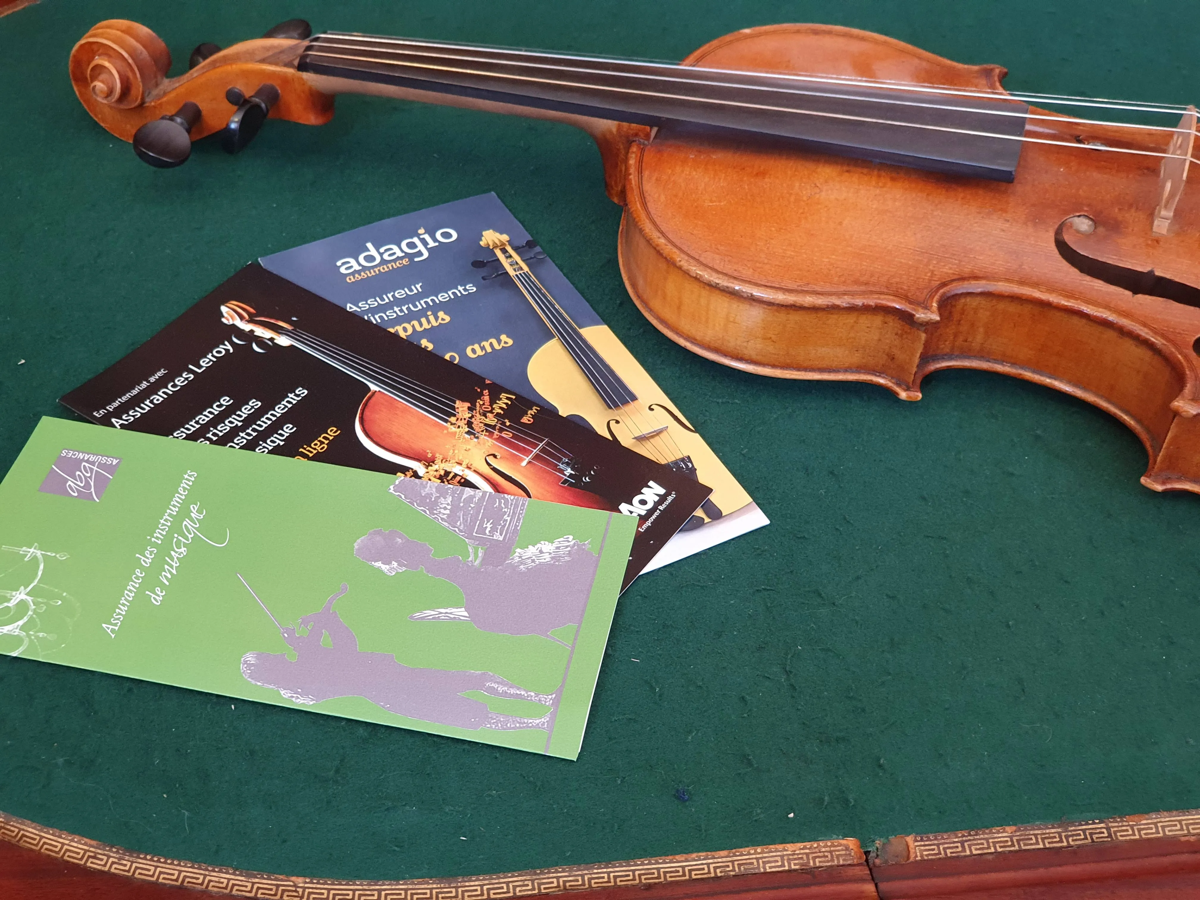 Violon posé sur une surface verte avec trois brochures d'assurance instruments de musique à côté.