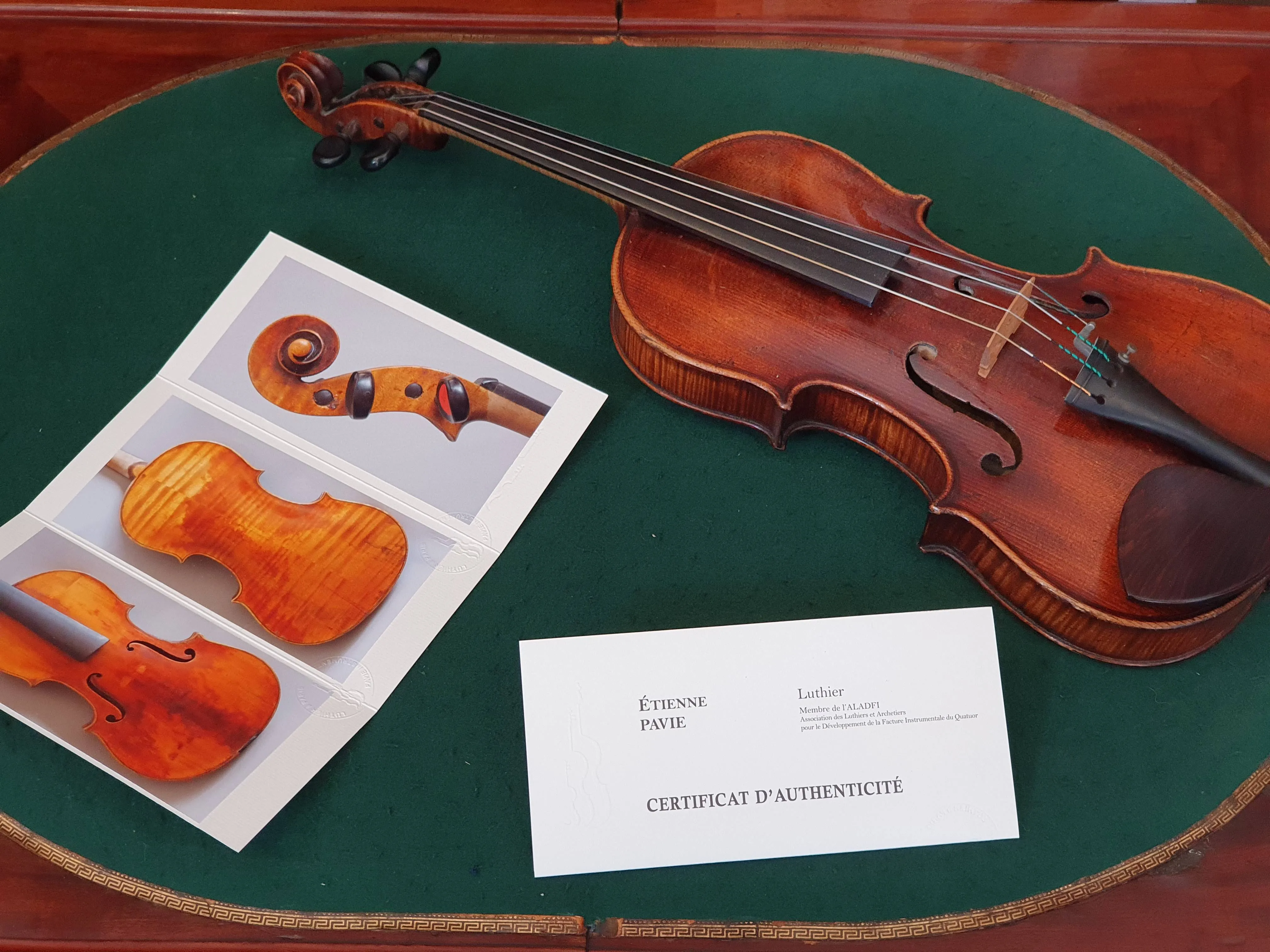 Un violon posé sur une table verte avec une carte de visite d'Étienne Pavie, luthier, et un certificat d'authenticité.