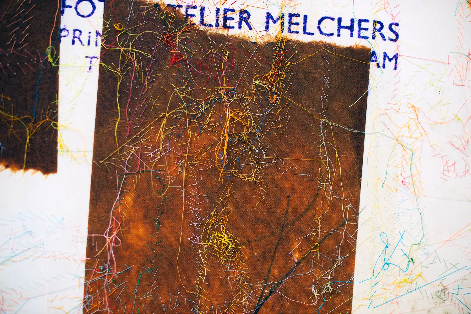 A richly layered work combining a photographic or painted base in grays and blacks with bold embroidered figures and faces in orange, yellow, red, magenta, and purple thread. Multiple expressive, child-like portraits overlap across the surface in Strik's characteristic technique of stitching on a photographic image.