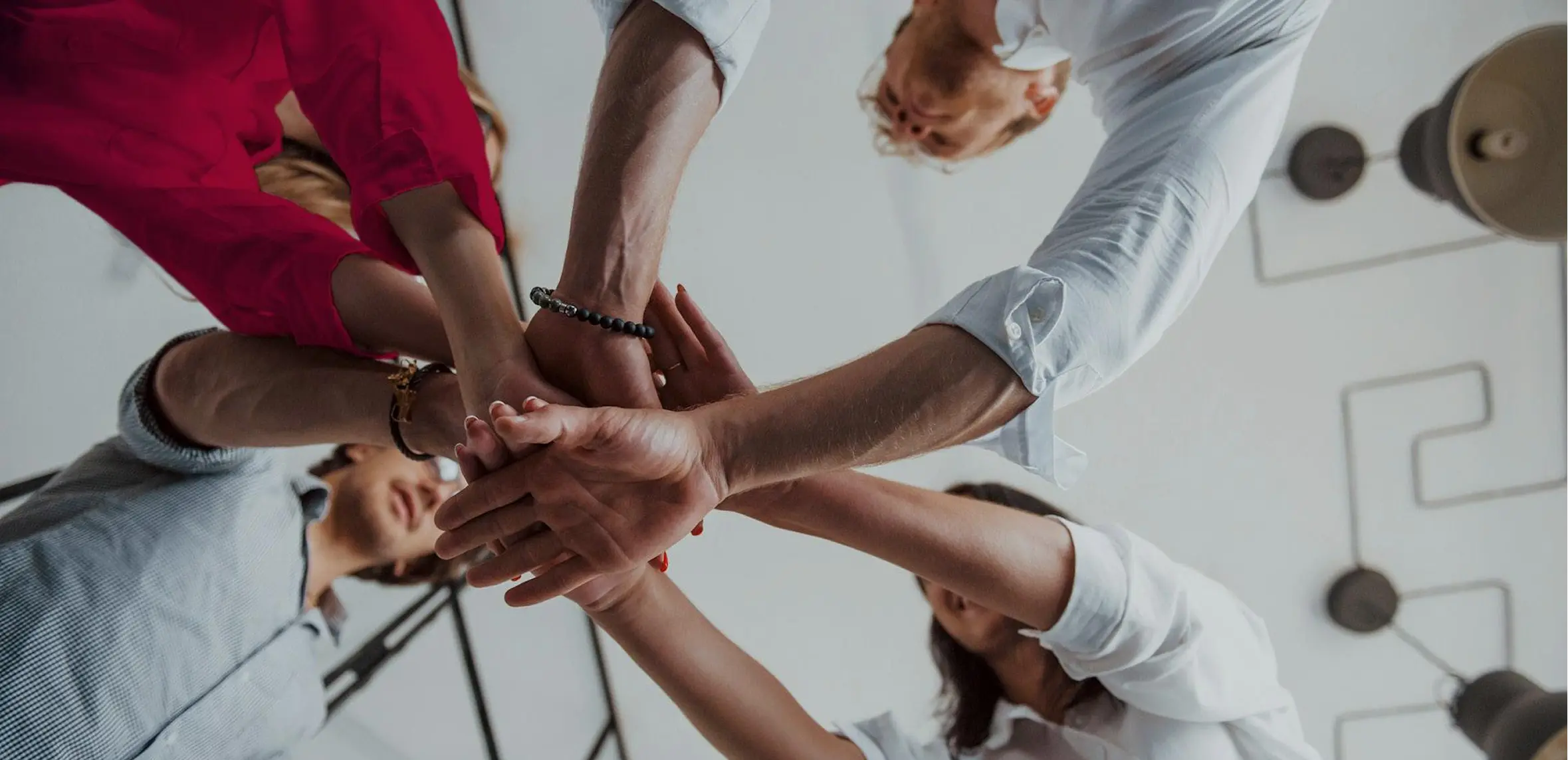 Group of people standing in a circle stacking their hands together in a teamwork gesture.