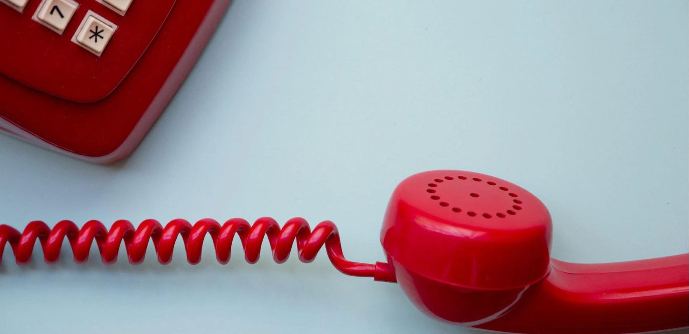 Close-up of a red vintage telephone handset and part of the keypad on a light surface.
