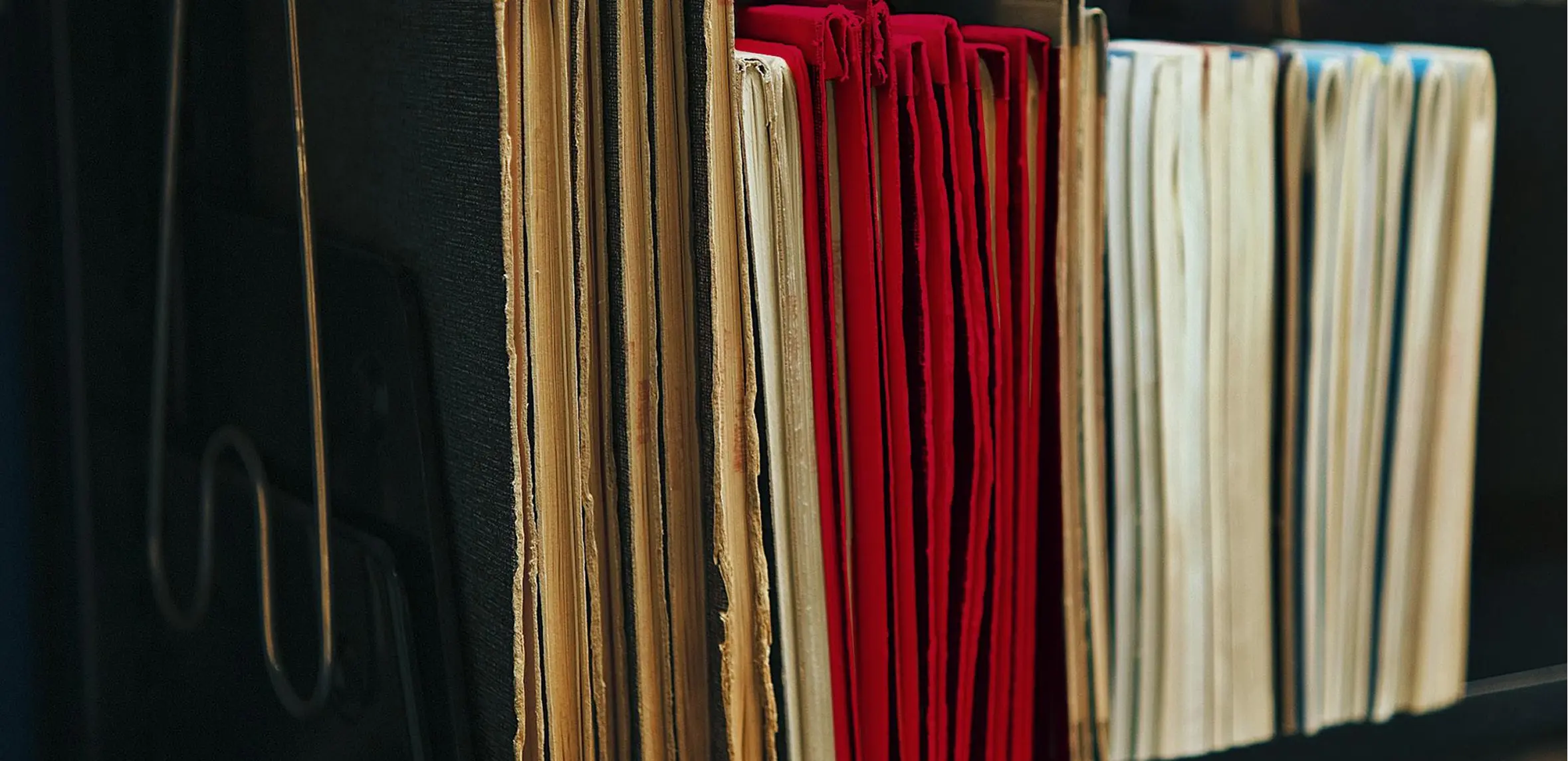 Close-up side view of worn paper folders in beige, red, and white colors organized vertically in a black file holder.