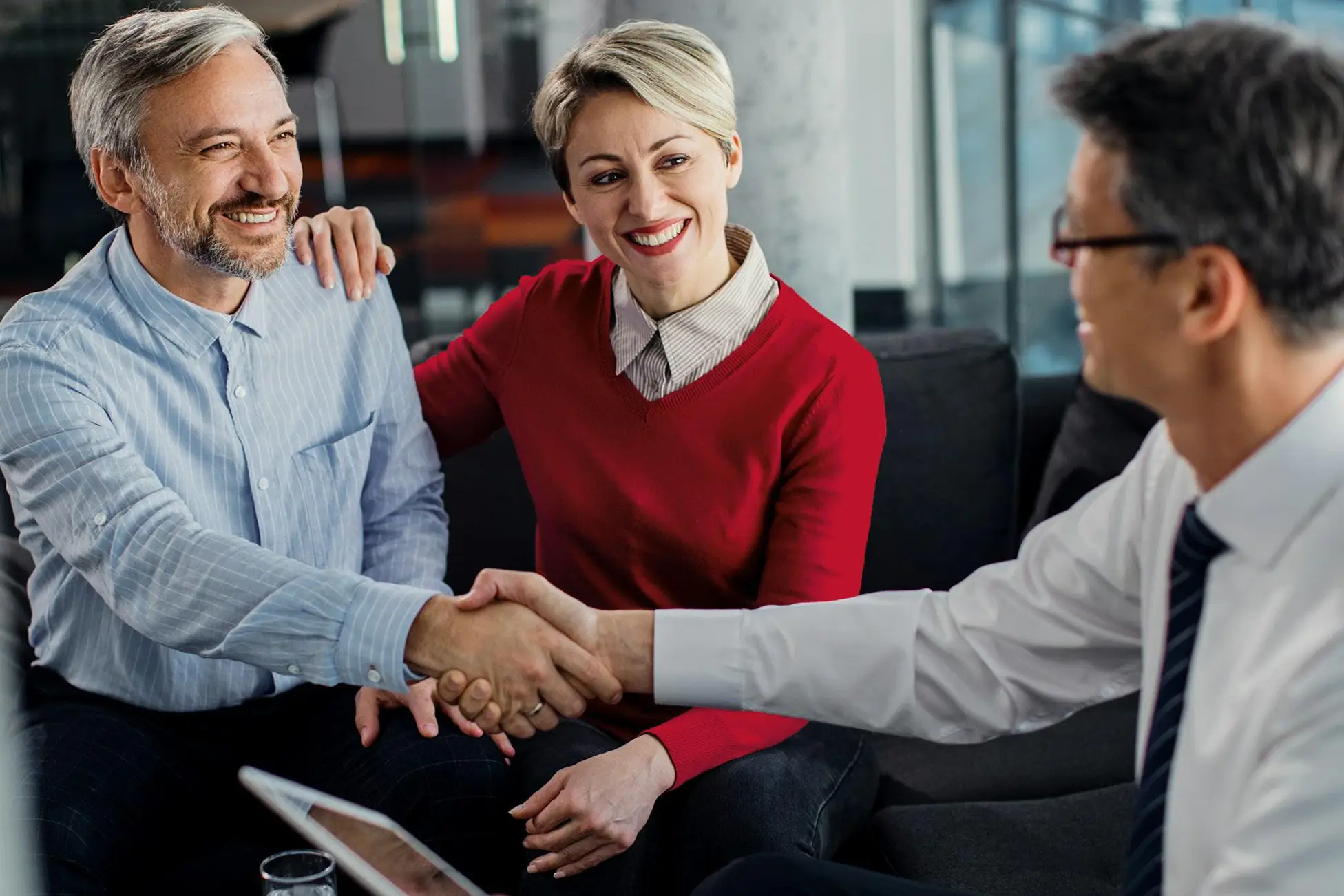 Smiling couple shaking hands with a man in a suit in a professional setting.