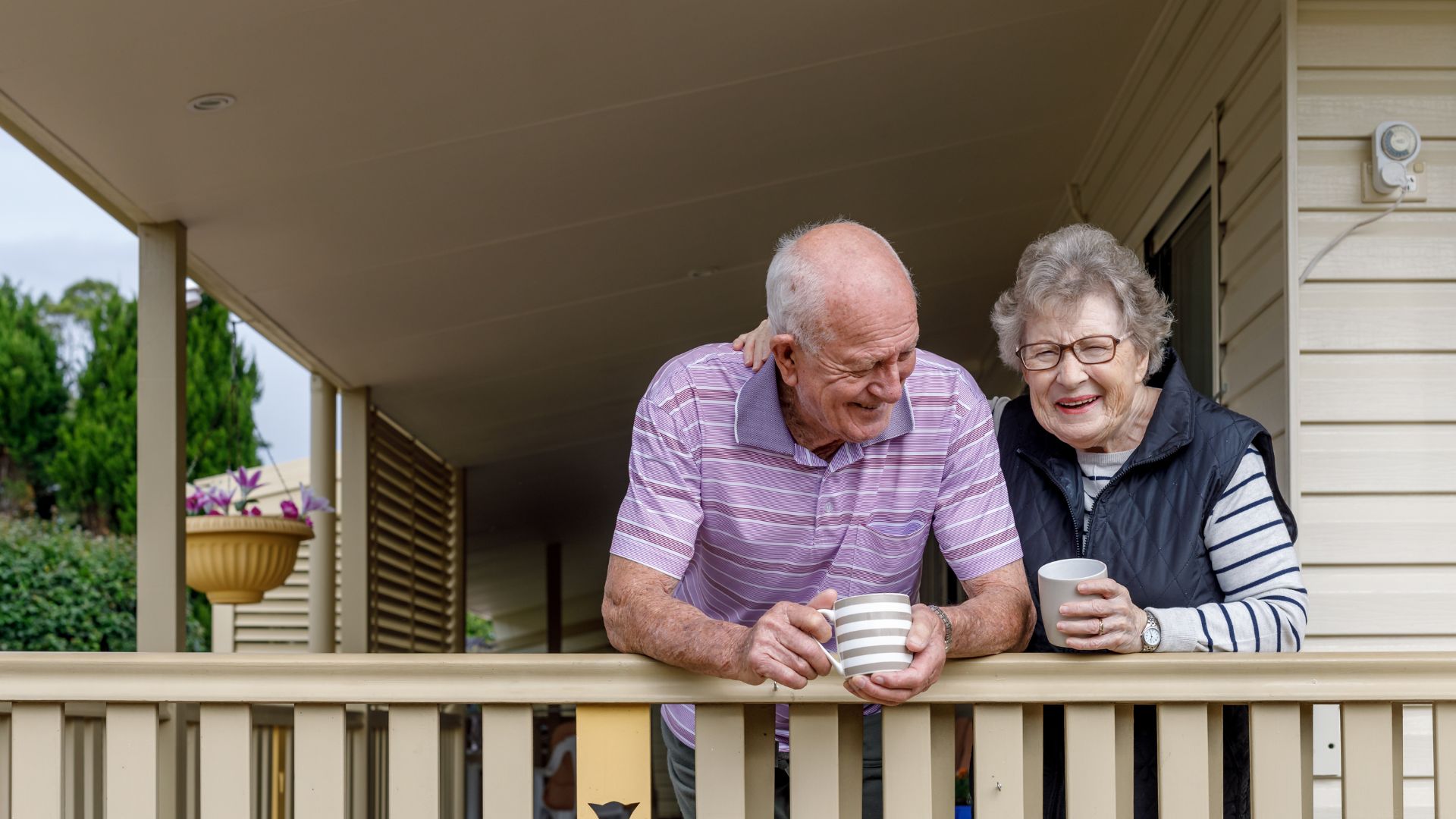 A senior couple shares coffee on their balcony in a senior living community.