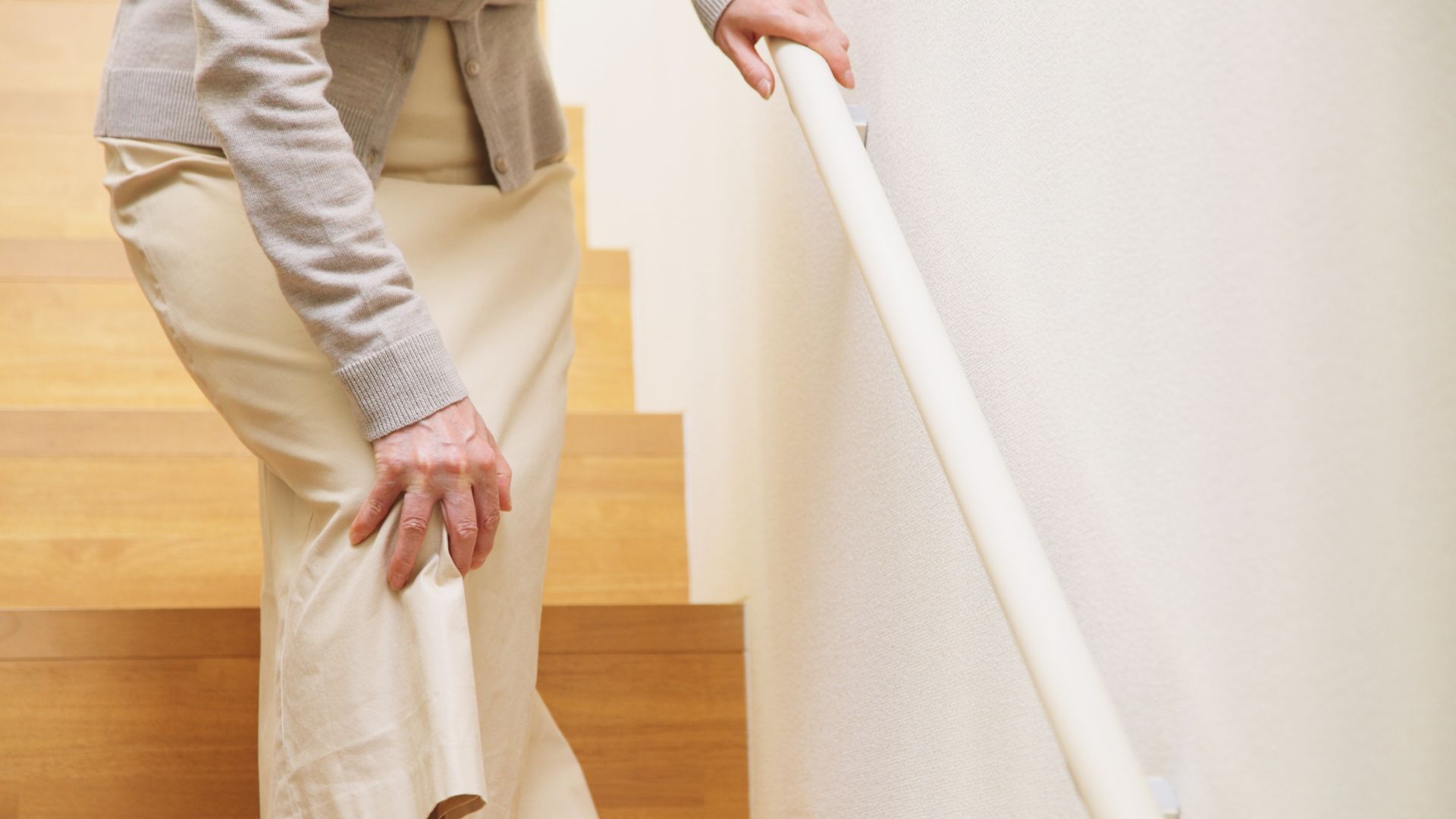 An older woman struggles with knee pain as she goes down the stairs in her home.