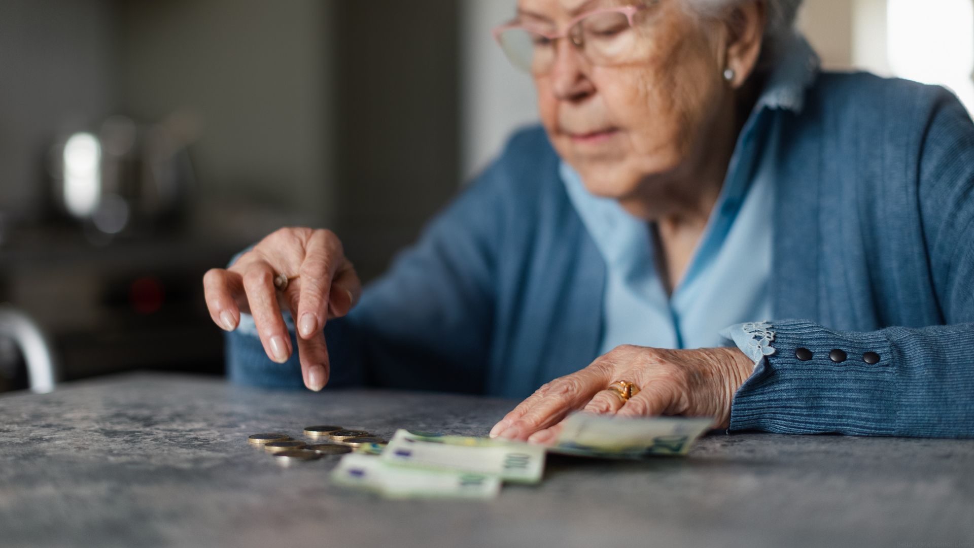 A senior woman counts her dollars and cents on the kitchen table.