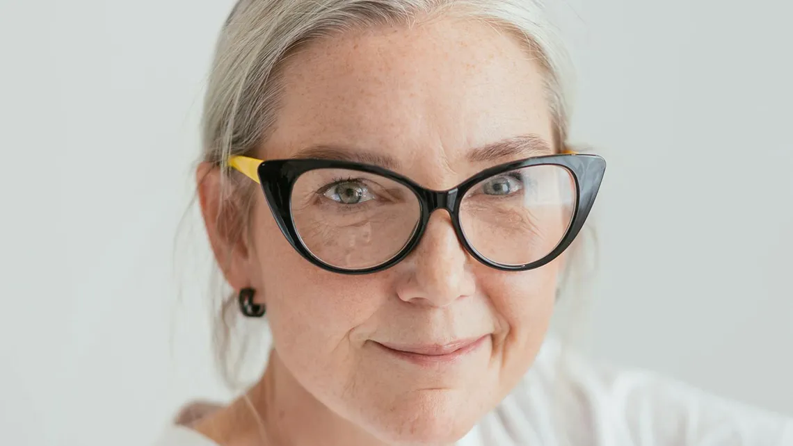 Smiling middle-aged woman with gray hair and black cat-eye glasses with yellow arms.