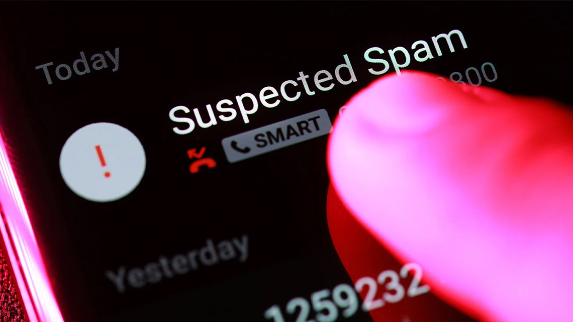 Close-up of a finger touching a smartphone screen displaying a call marked as Suspected Spam.