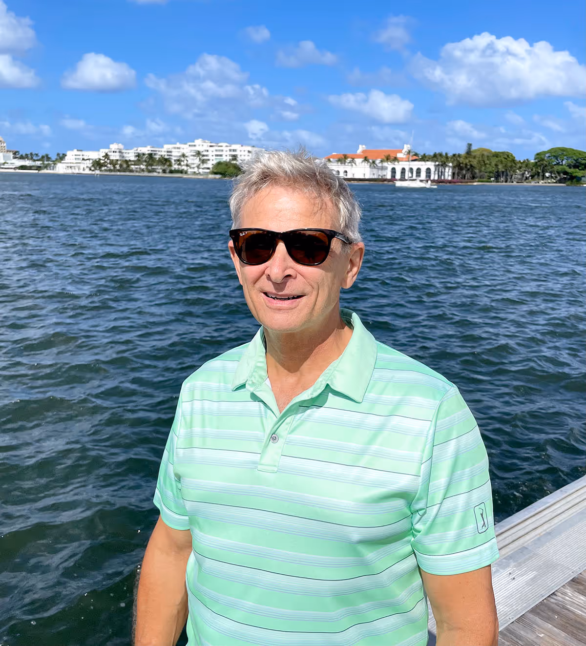 Smiling middle-aged man with short gray-blond hair wearing a dark gray collared shirt against a plain background.