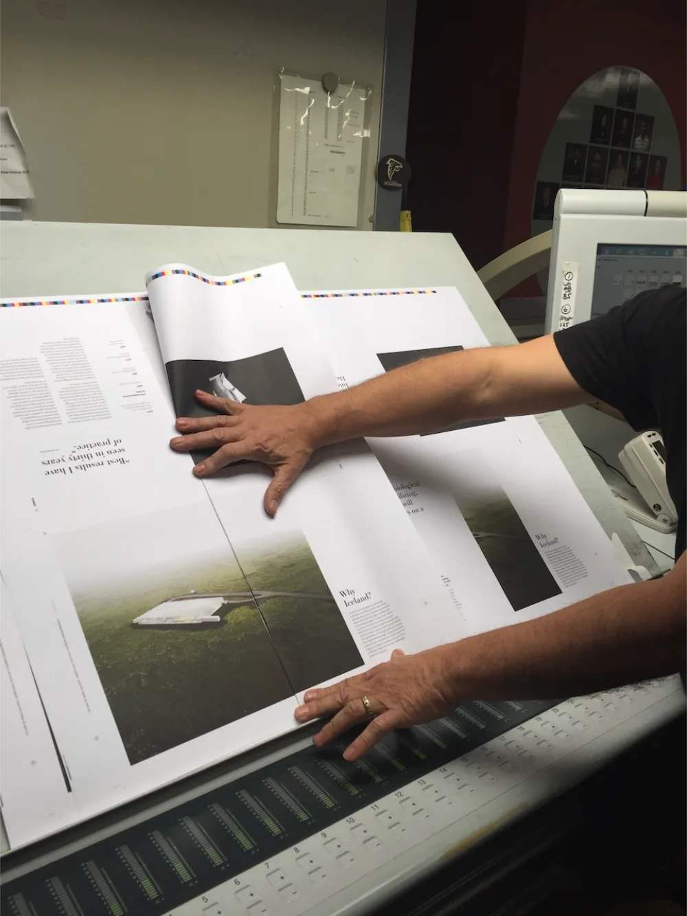 Person inspecting large printed sheets of magazine pages on a print press table.
