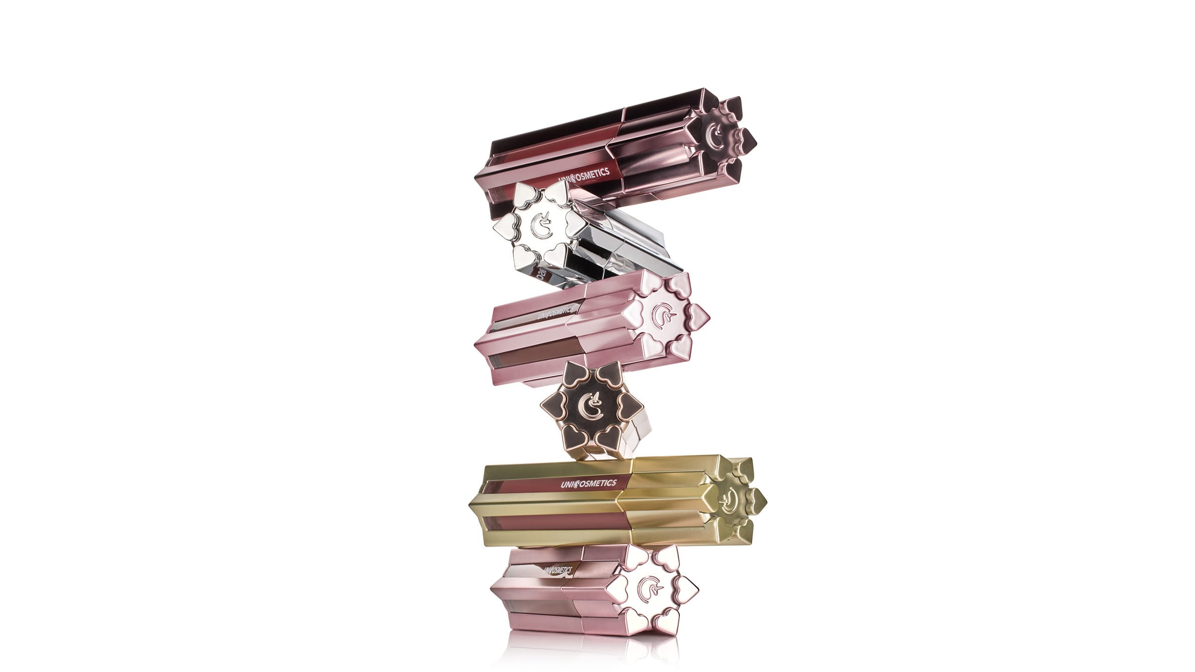 Stack of five uniquely shaped UNICOSMETICS lipsticks with heart details on caps in various metallic colors.