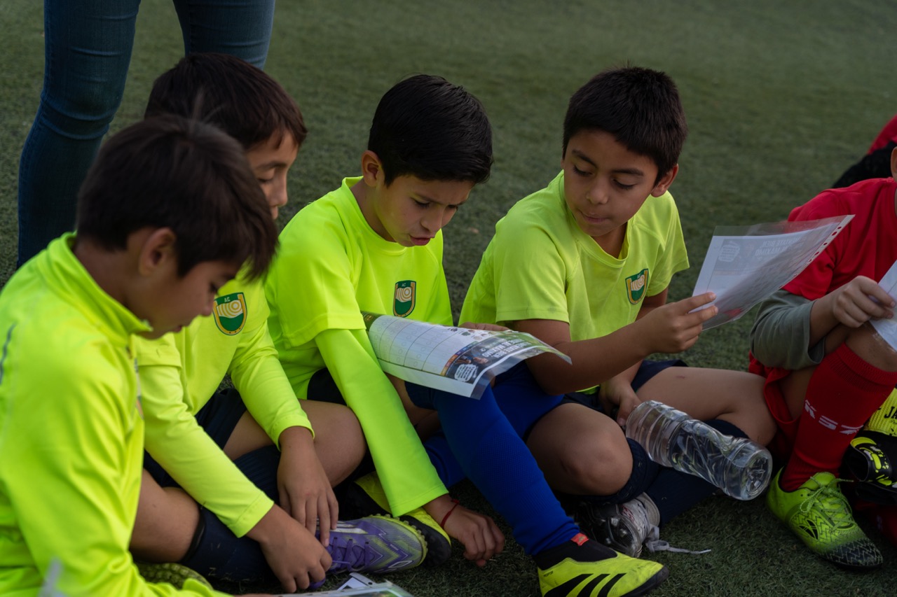 Niños de la academia leyendo material educativo en la cancha