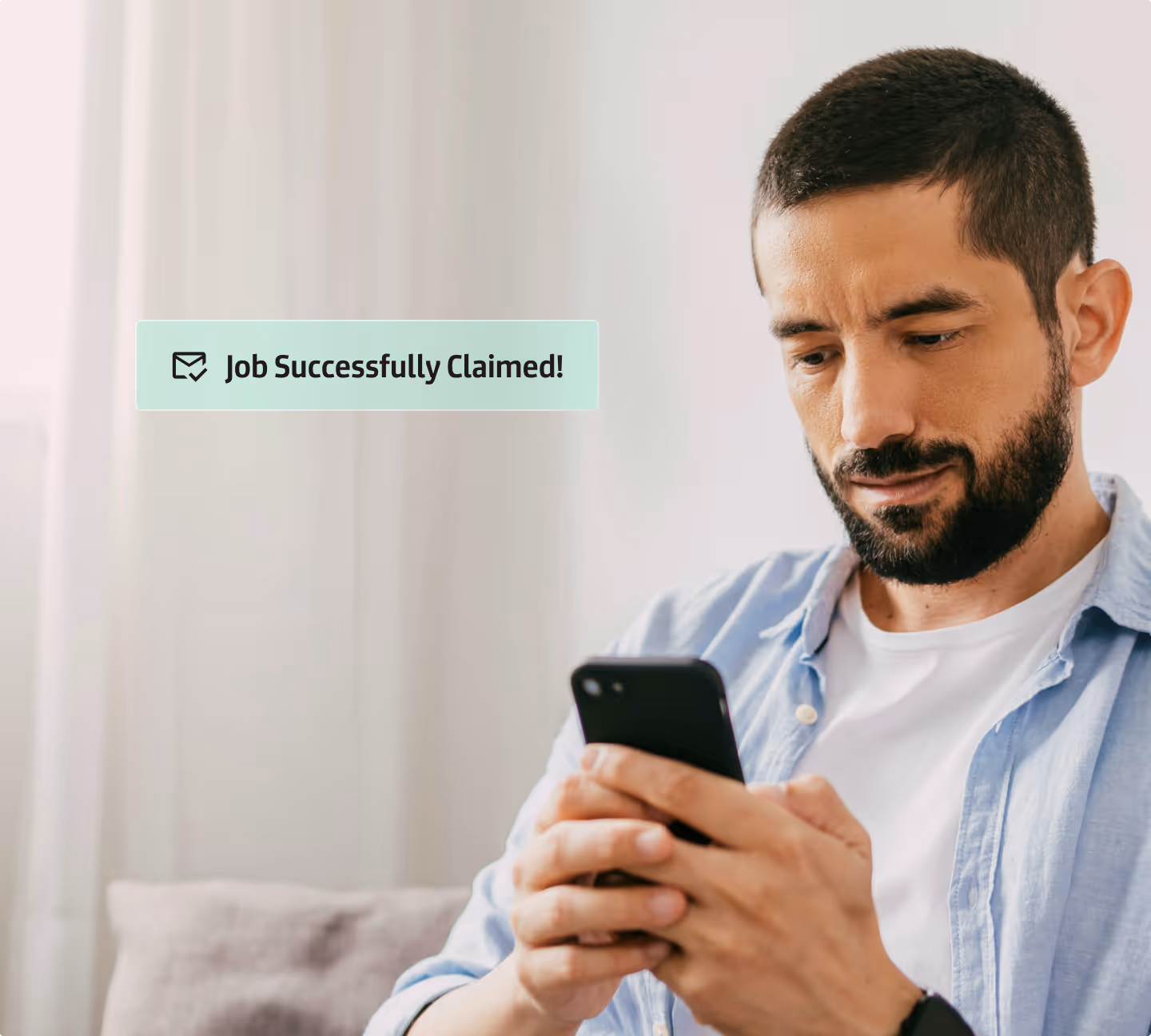 Man with beard and blue shirt looking at phone with a message saying Job Successfully Claimed.
