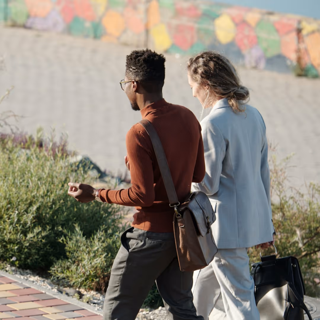 Two business professionals walking outdoors carrying bags, engaged in conversation.