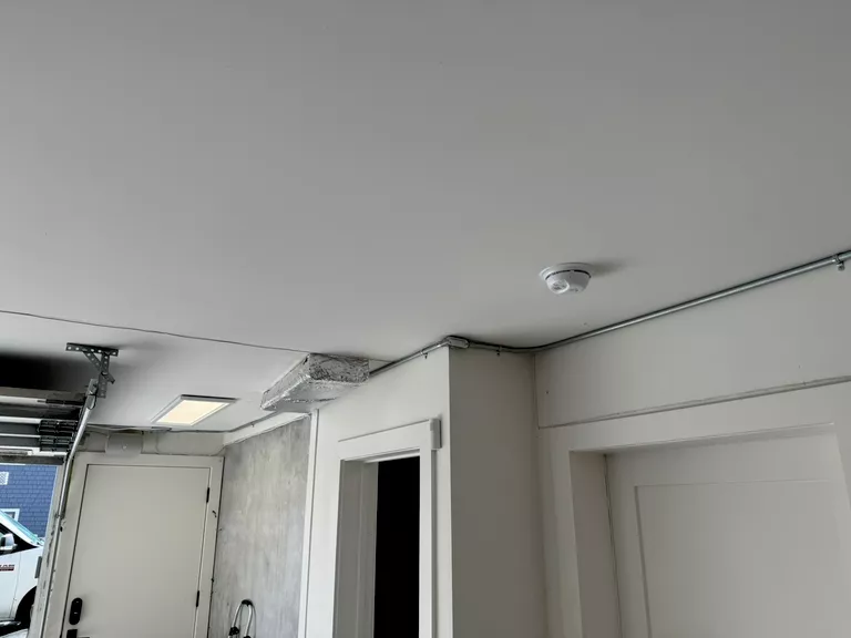 Indoor corner showing white ceiling, walls, a smoke detector, and doors with garage mechanism visible.