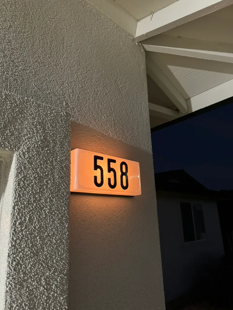 Illuminated house number sign showing 558 mounted on a textured wall at dusk.