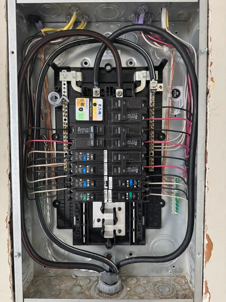 Electrical breaker panel with labeled circuit breakers and organized wiring inside a metal enclosure.
