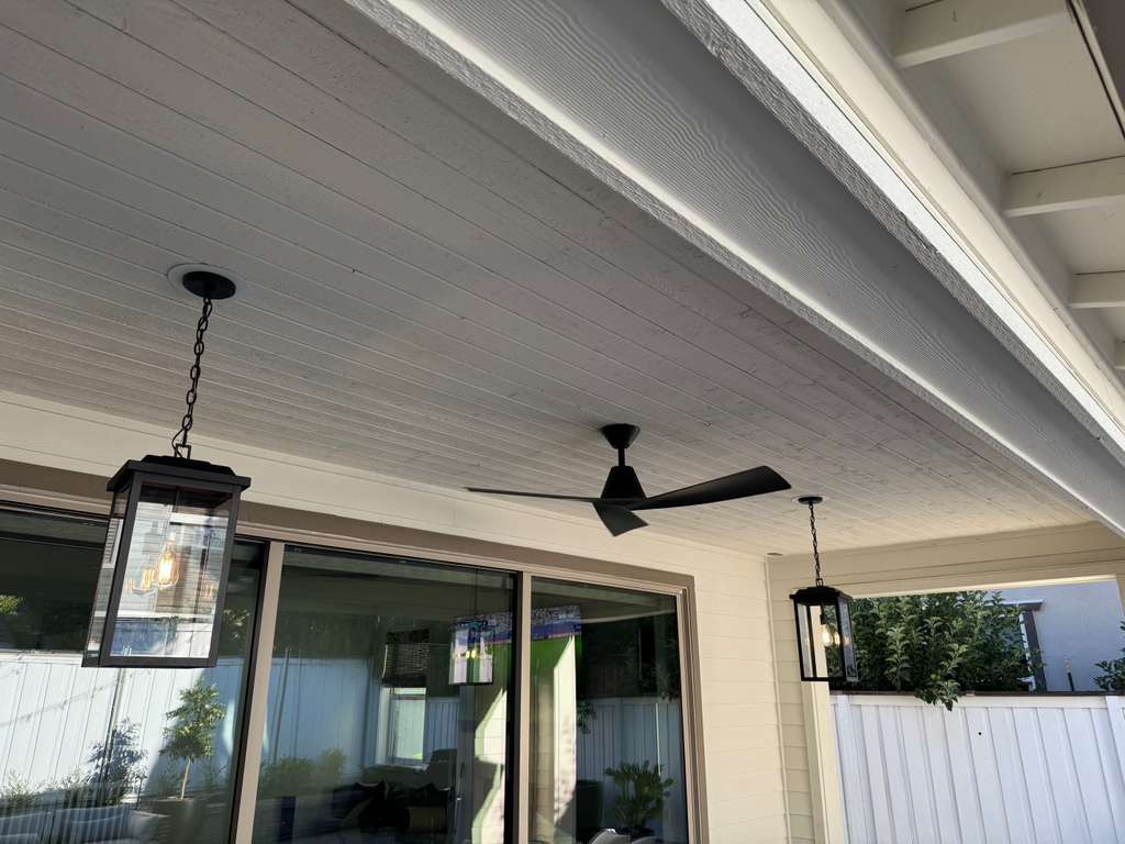 Ceiling fan with two hanging lantern lights on a covered patio with glass doors and white fence.