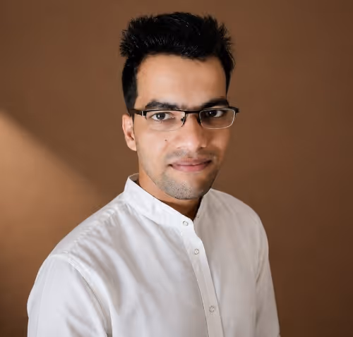 Man wearing glasses and a white button-up shirt against a plain brown background.