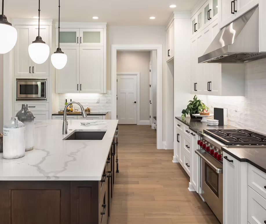 Modern kitchen with white cabinets, marble island, stainless steel stove, and hanging pendant lights.