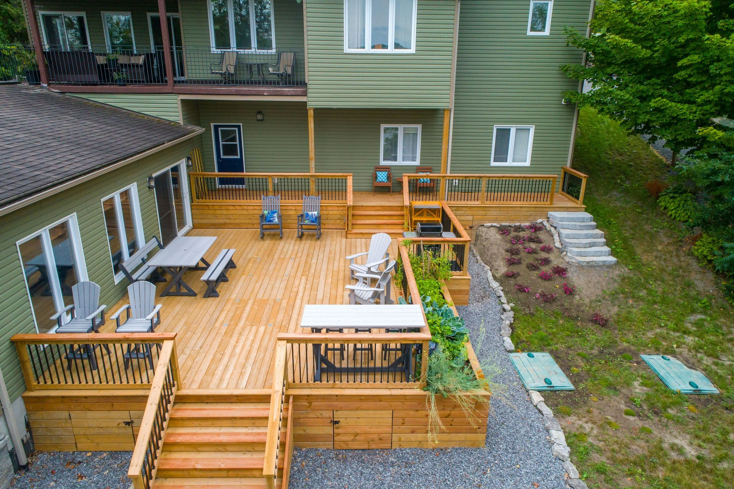 Spacious wooden backyard deck with chairs, tables, planter boxes, and stairs leading to yard and house.