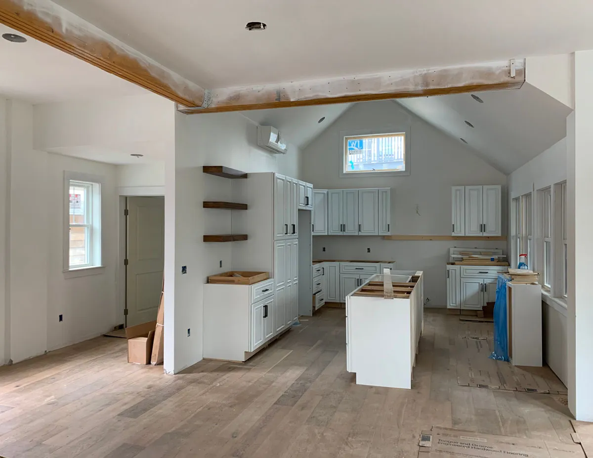 New kitchen under construction with white cabinets, open shelves, island base, and wood floors.