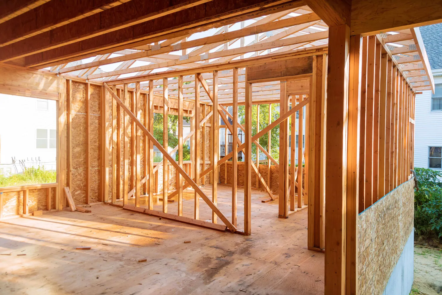 Wooden framing structure of a house under construction with sunlight casting shadows inside.