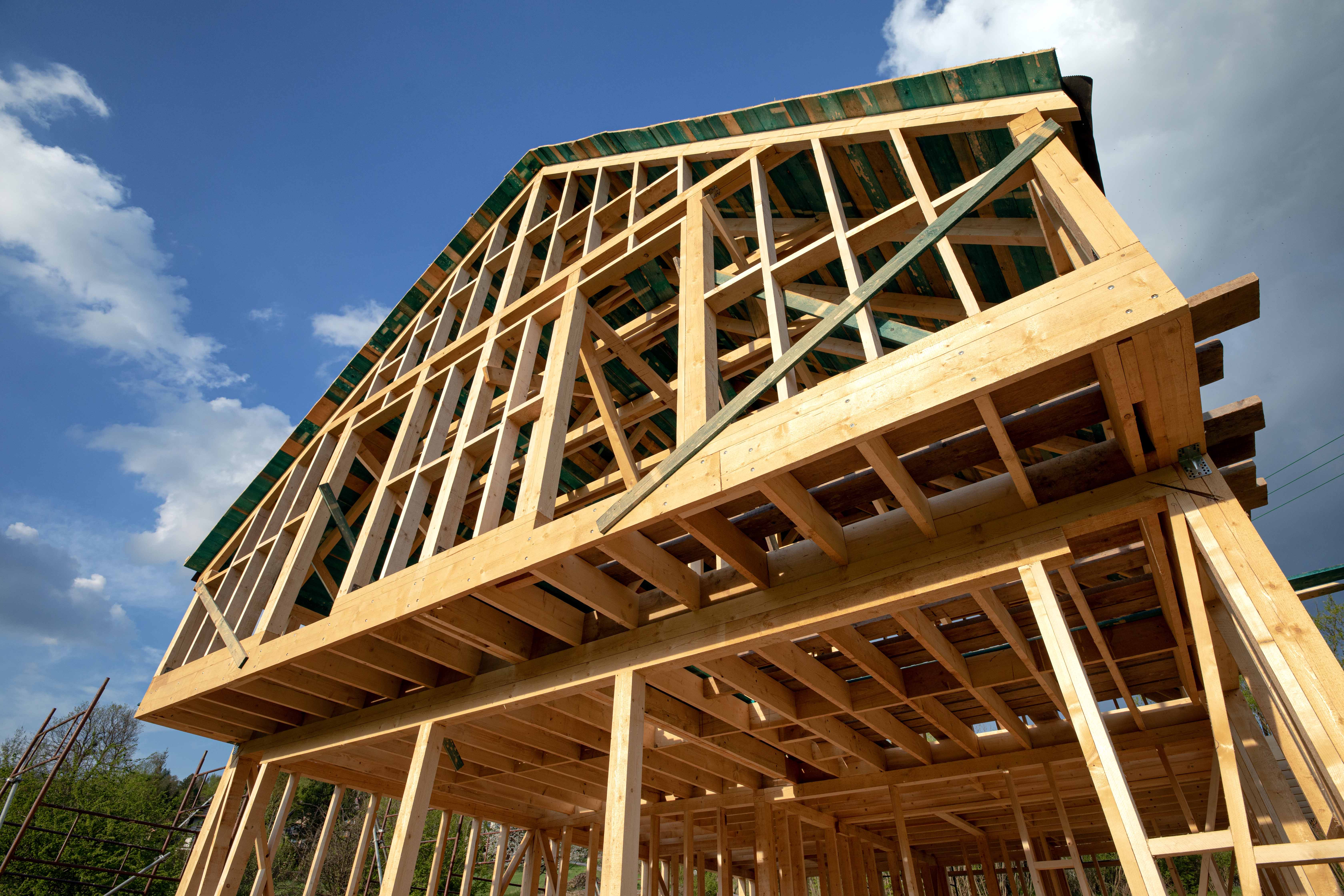 Wooden frame structure of a house under construction against a blue sky with clouds.