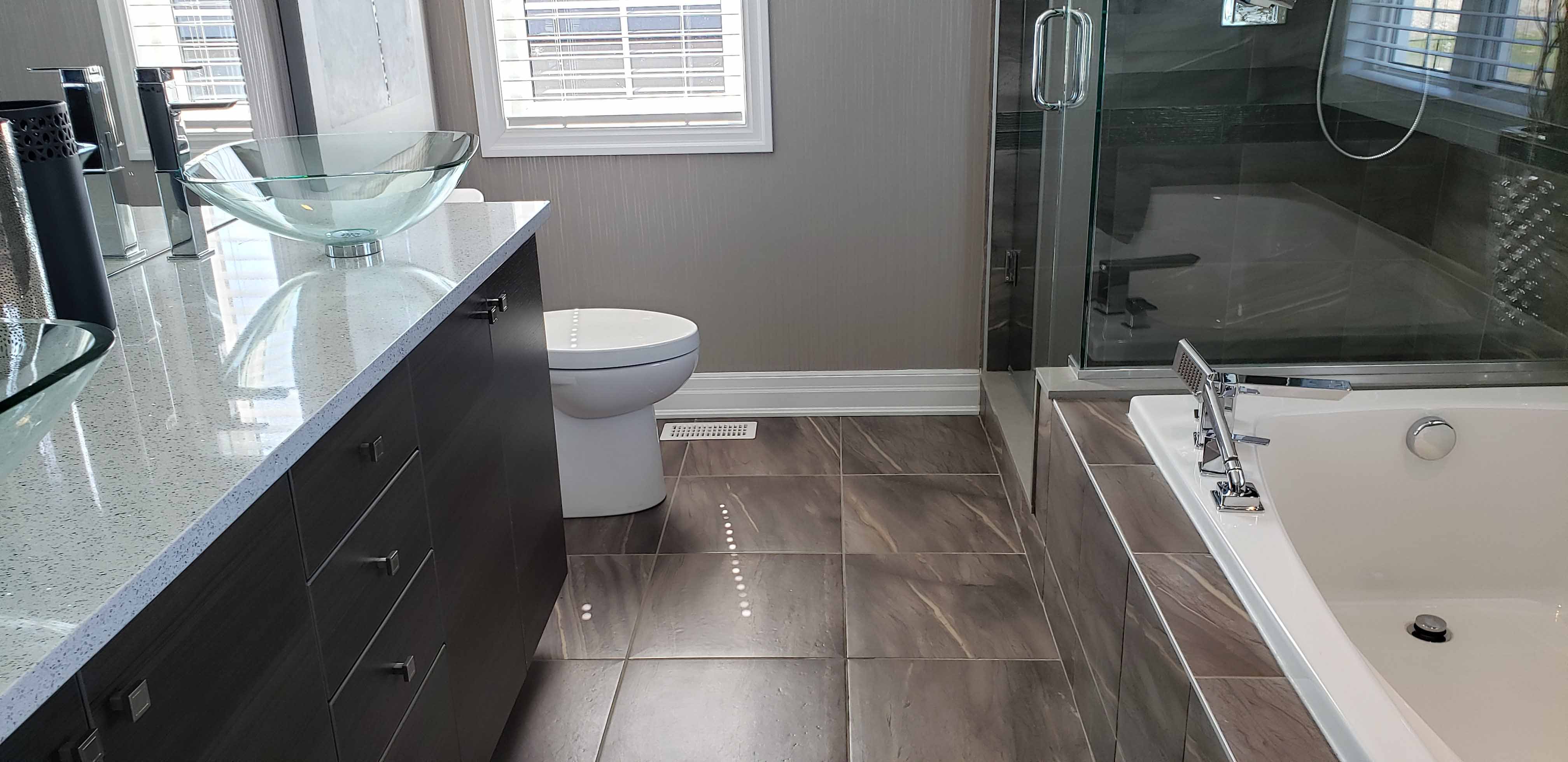 Modern bathroom with glass vessel sinks, dark cabinetry, white toilet, and a bathtub with chrome fixtures.