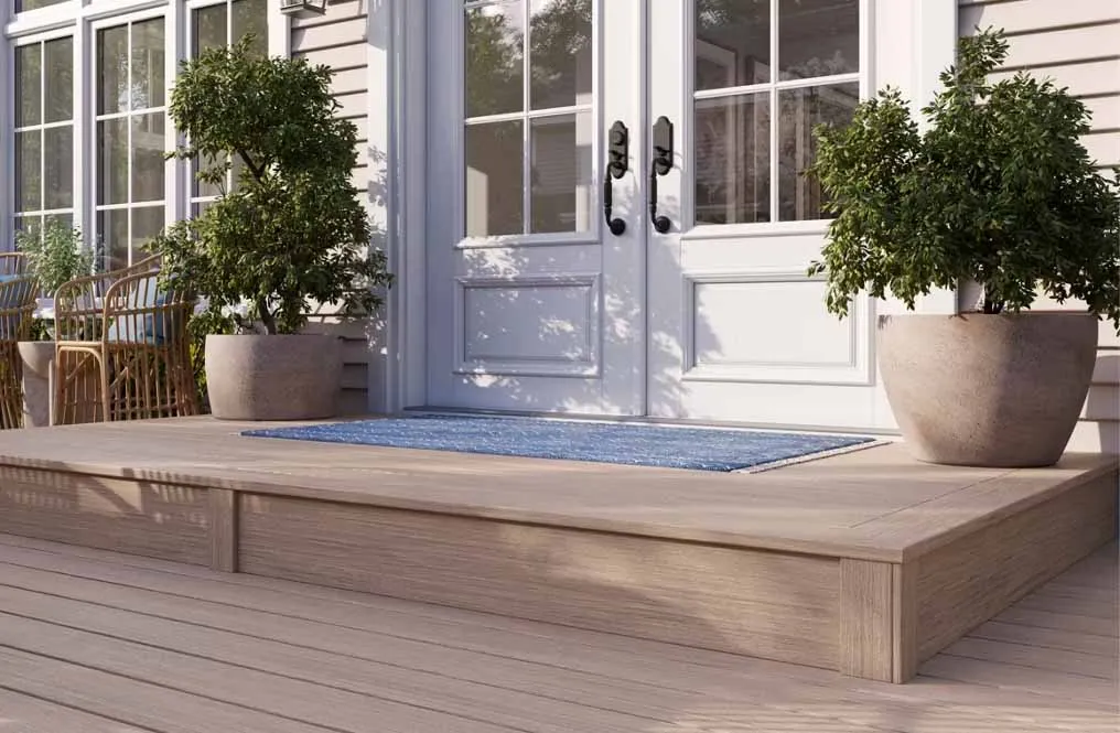 Wooden front porch with potted plants and double glass doors with black handles.