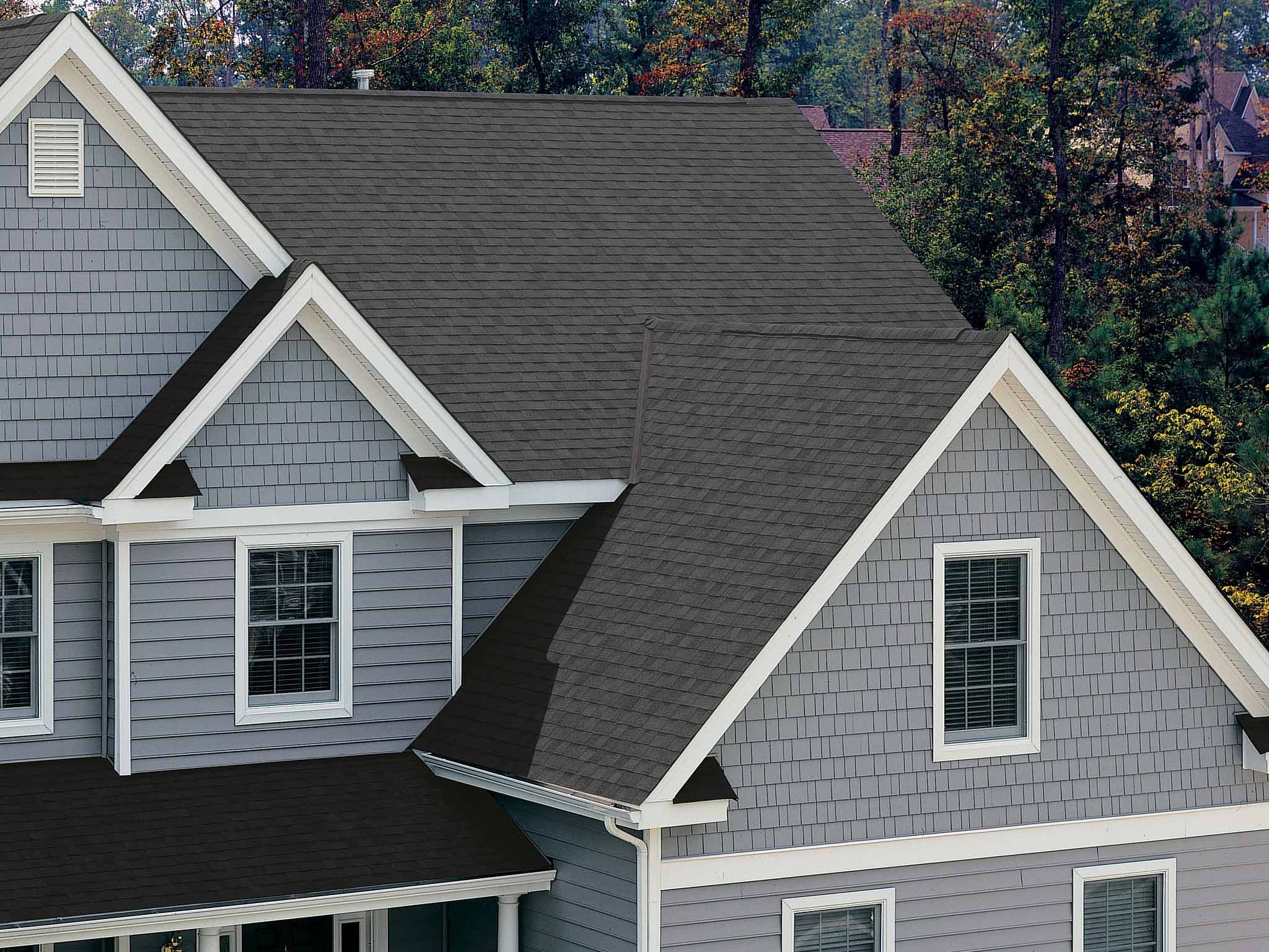 Gray house with multiple steep gray shingled roofs and white window frames surrounded by trees.