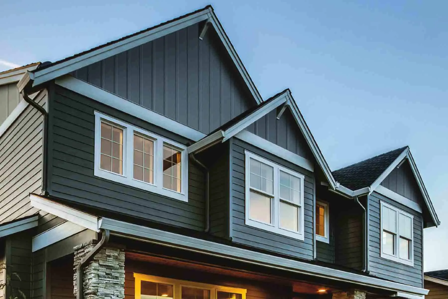 Dark gray composite siding on a modern two-story house with white-trimmed windows at dusk.