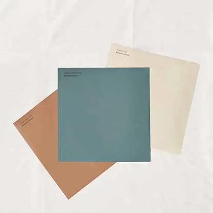 Three square paint swatches in muted blue, cream, and terracotta colors on a white fabric background.
