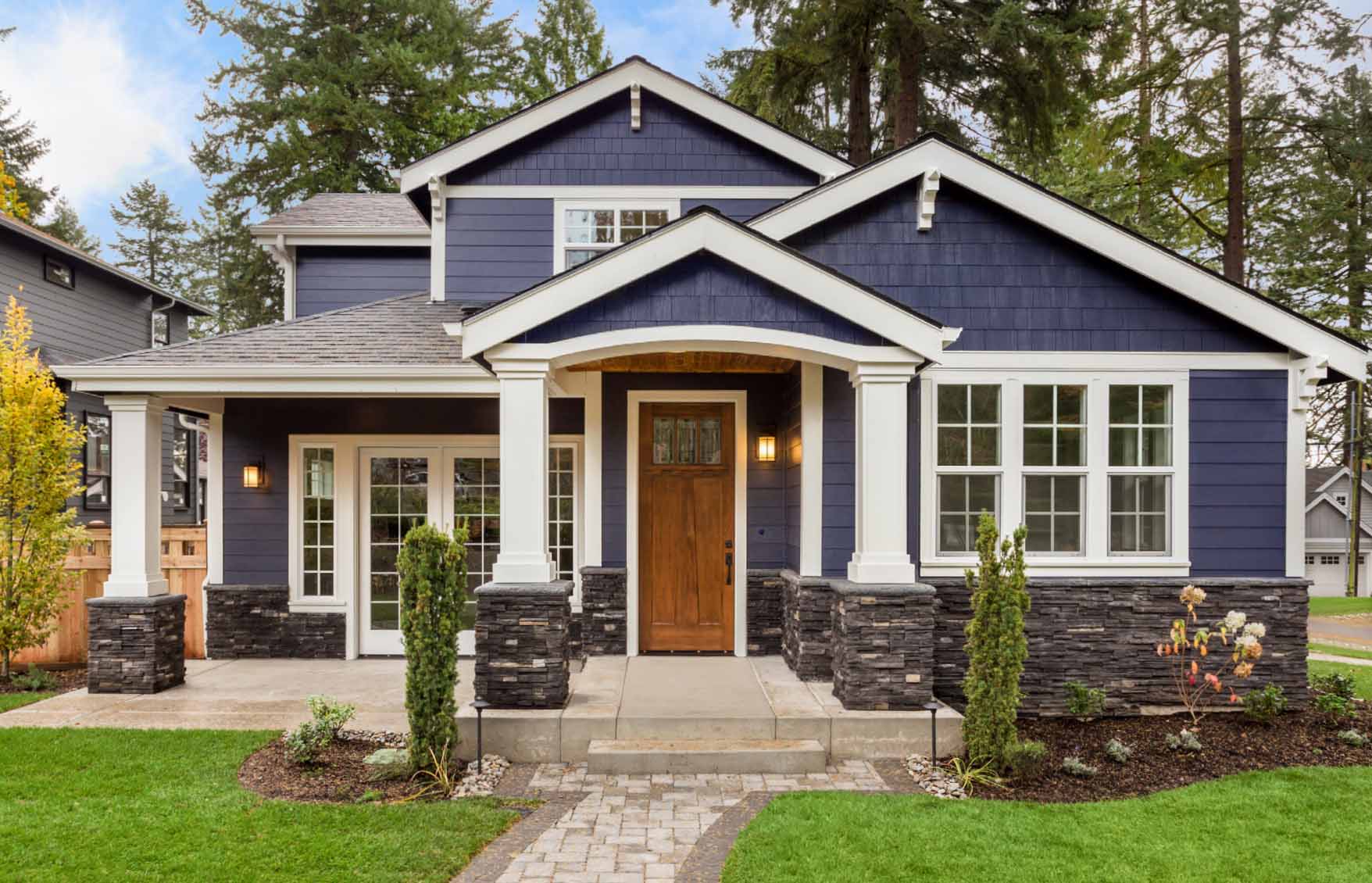 Two-story blue house with white trim, stone accents, front porch, and landscaped yard.