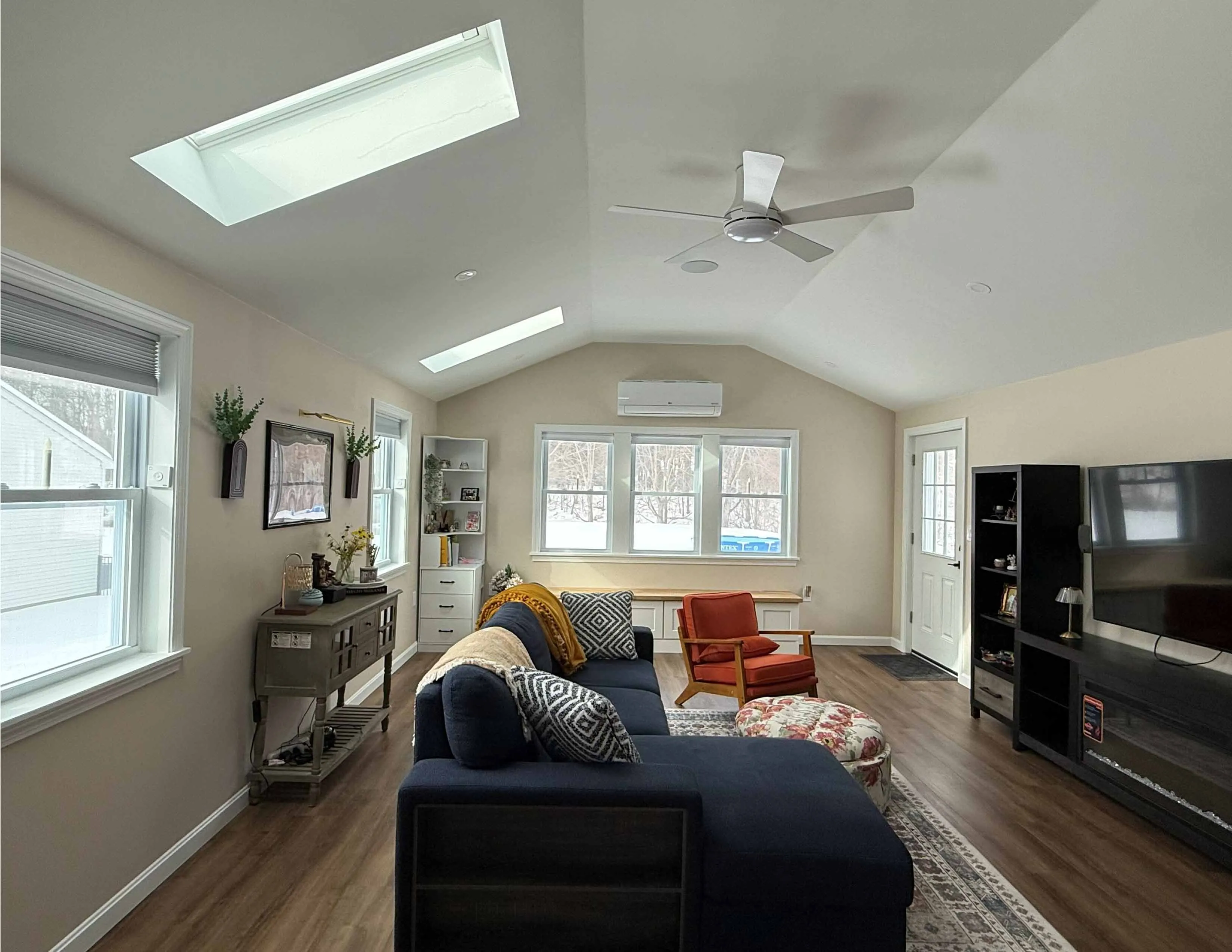 Bright living room with skylights, ceiling fan, navy sofa, orange chair, and wood floor.