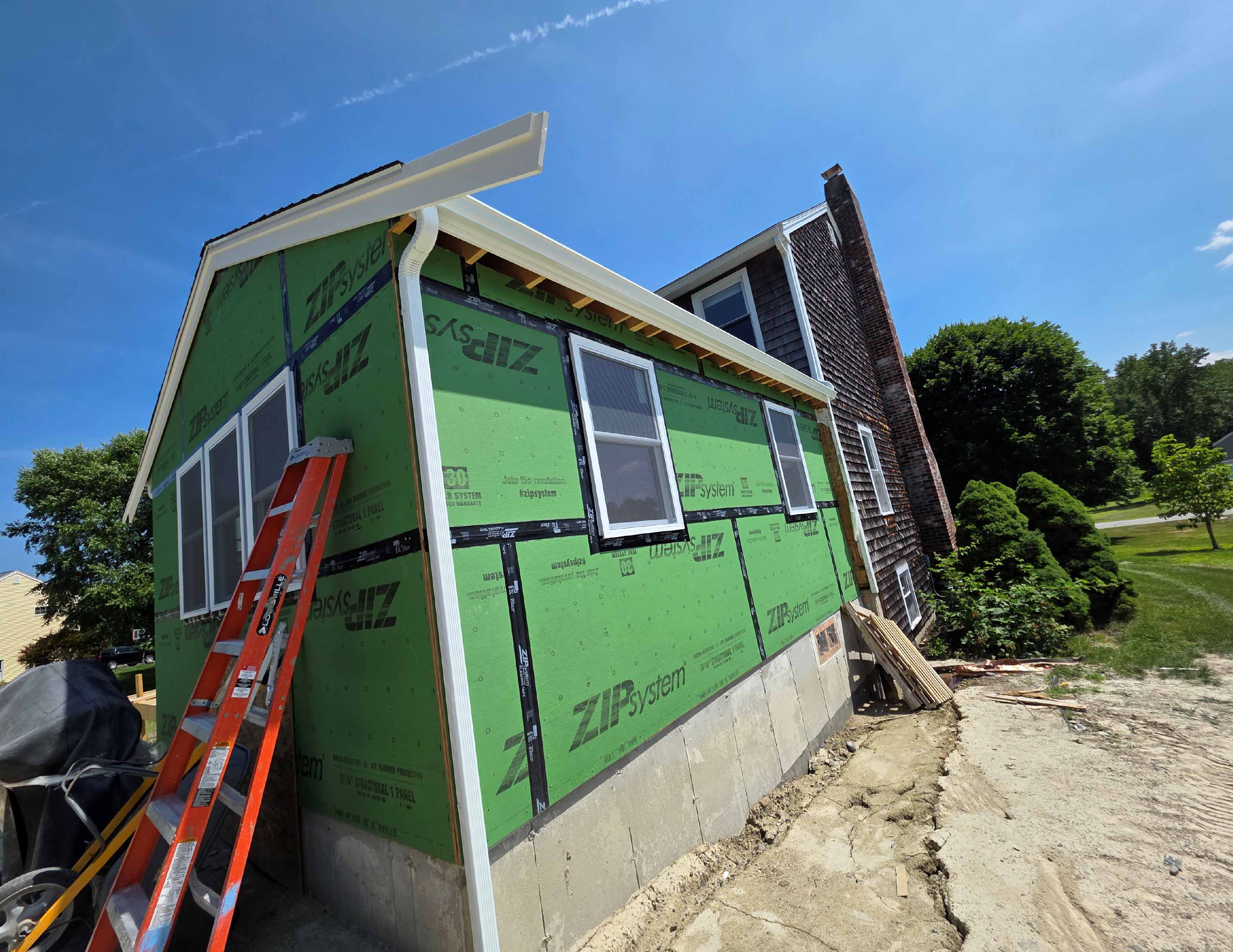 House extension under construction with green ZipSystem panels and an orange ladder leaning on it.