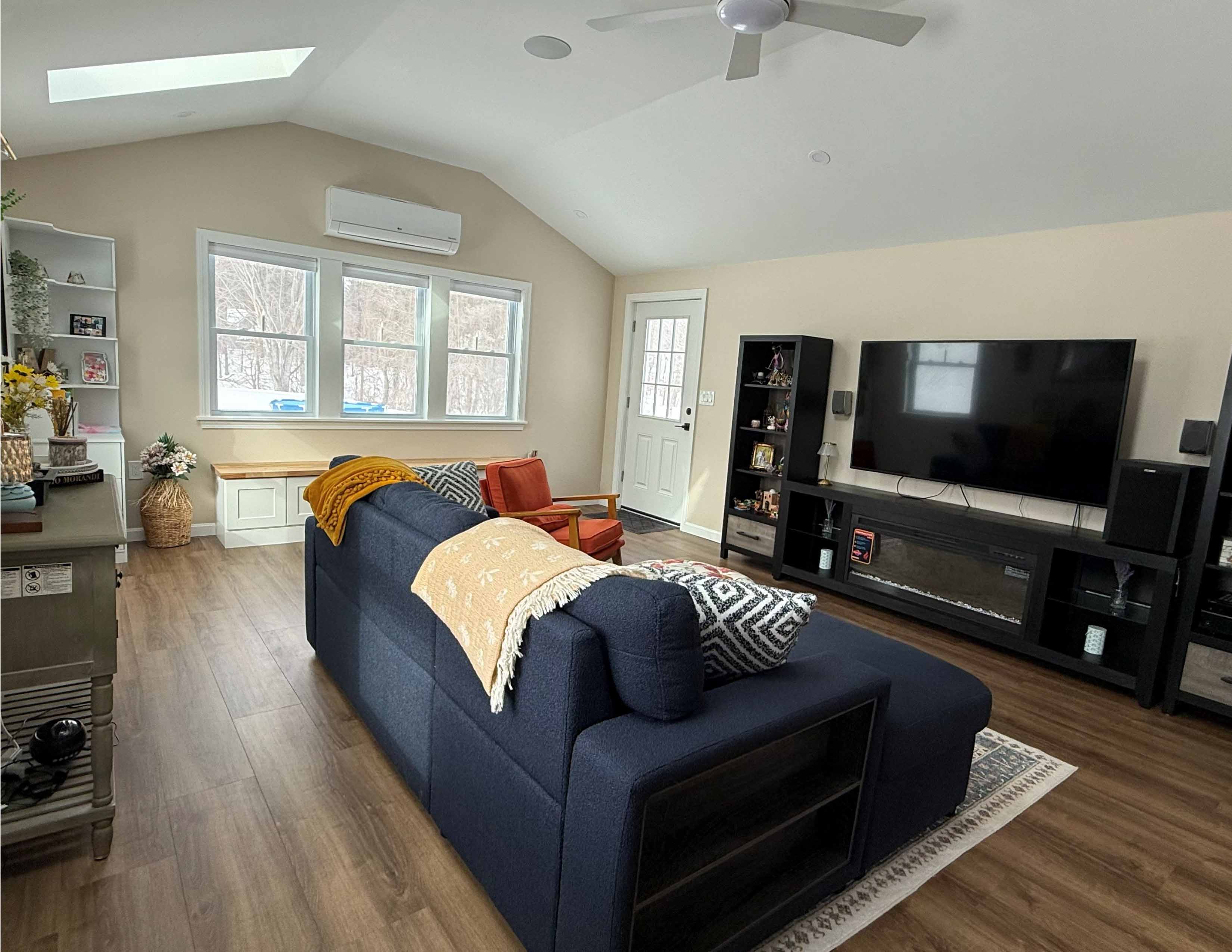 Modern living room with navy sofa, orange armchair, TV on black stand, and large windows.