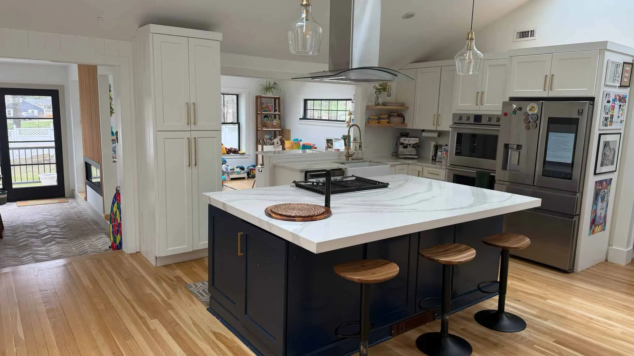 Modern kitchen with white cabinets, navy island with marble countertop, wooden stools, and stainless appliances.