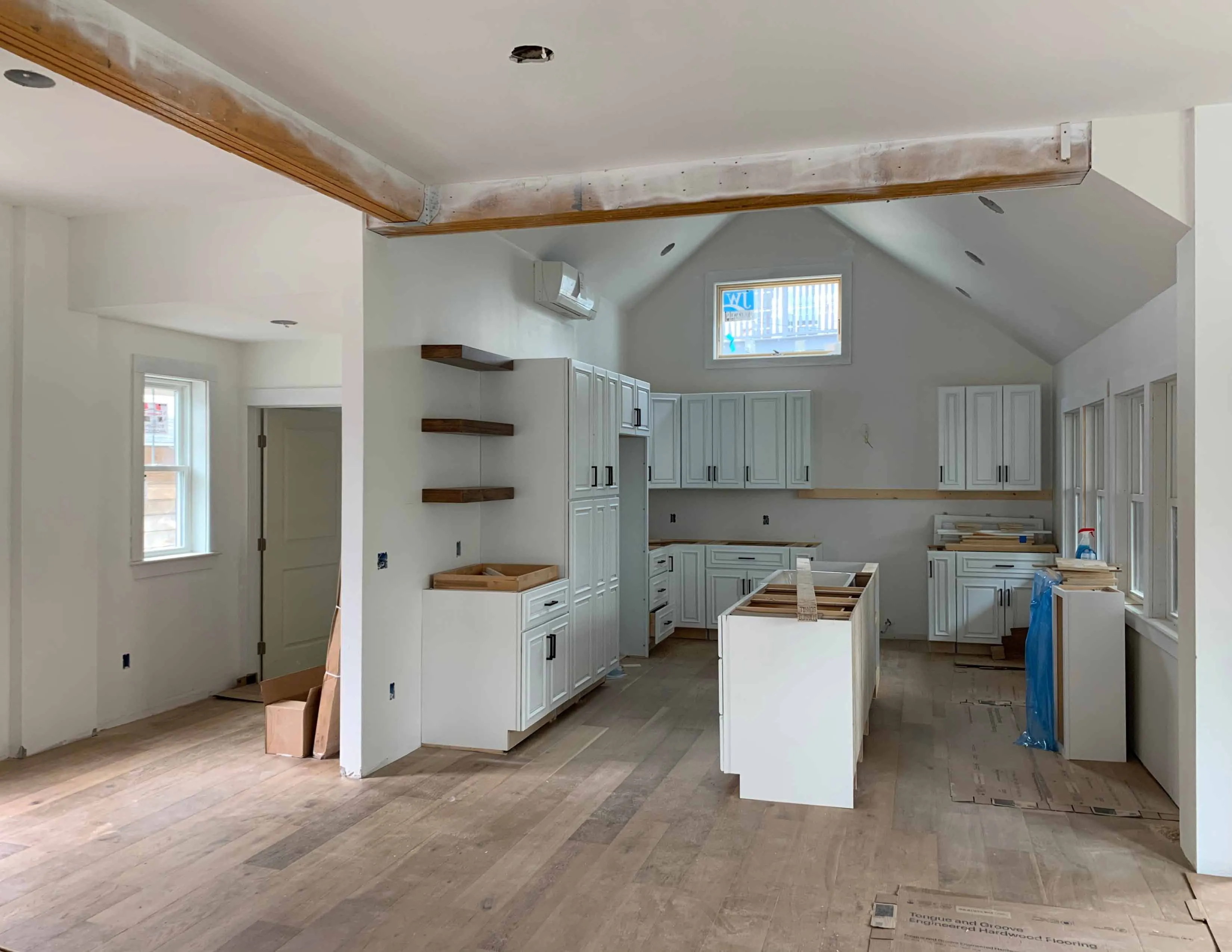 Modern kitchen under construction with white cabinets, wooden shelves, island, and hardwood floors.