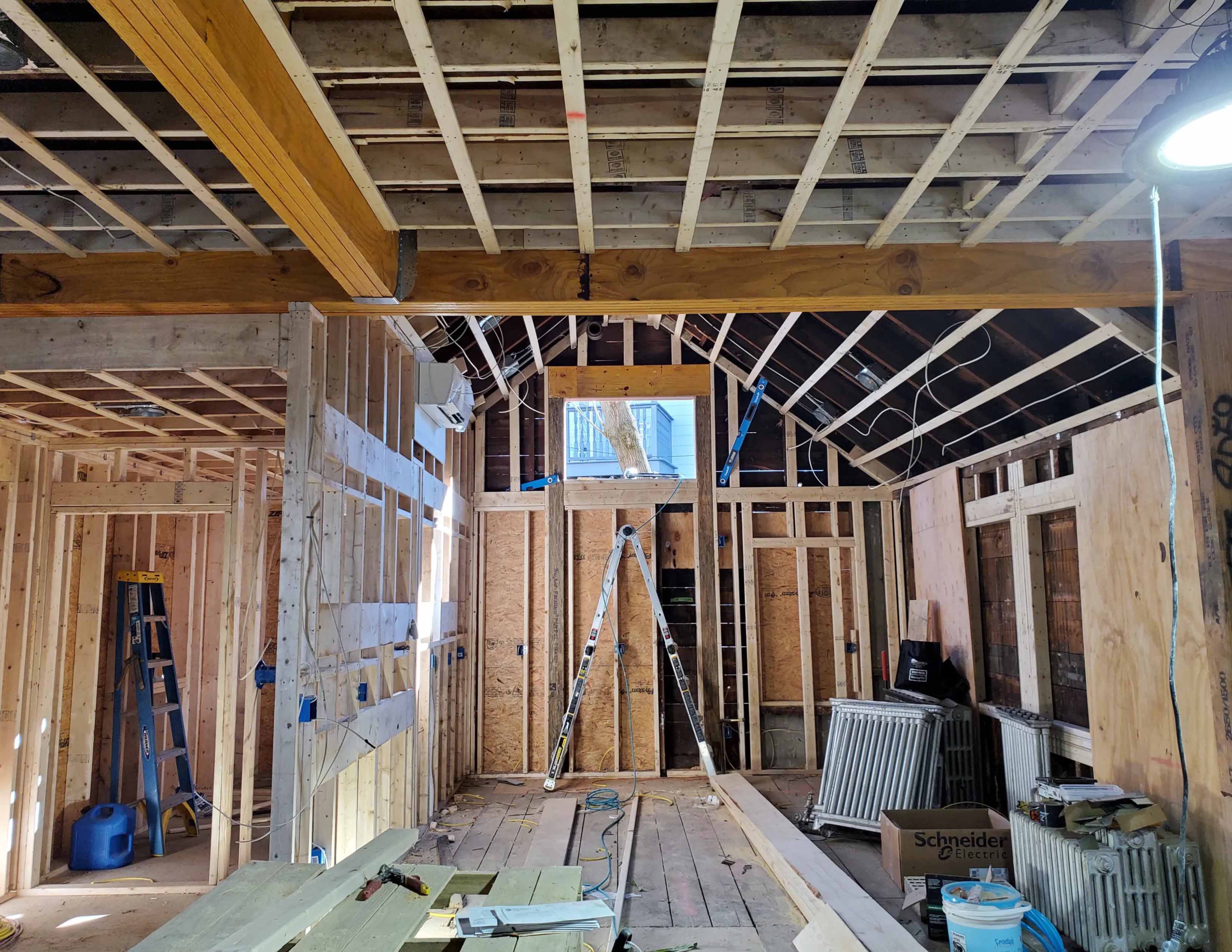 Interior of a wooden structure under construction with exposed beams, ladder, and construction materials.