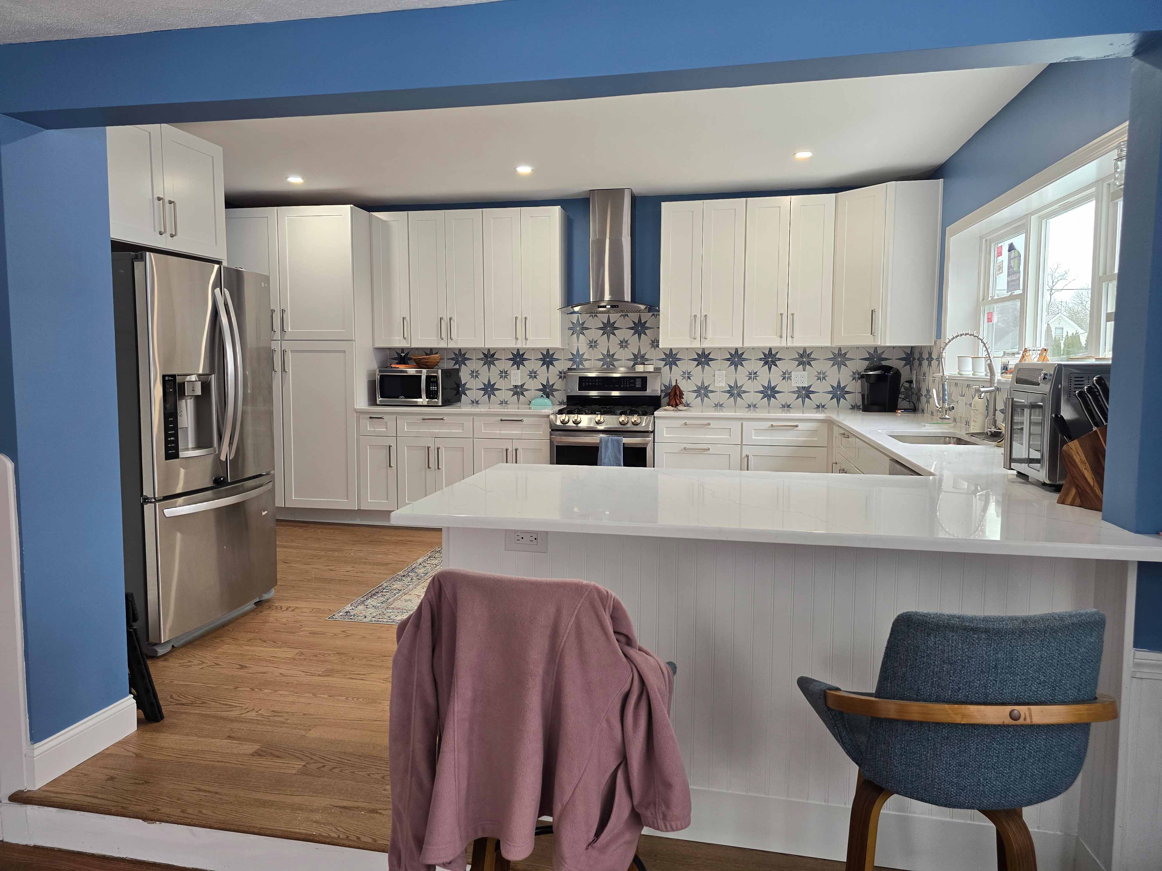 Modern kitchen with blue walls, white cabinets, patterned tile backsplash, and a breakfast bar with two chairs.