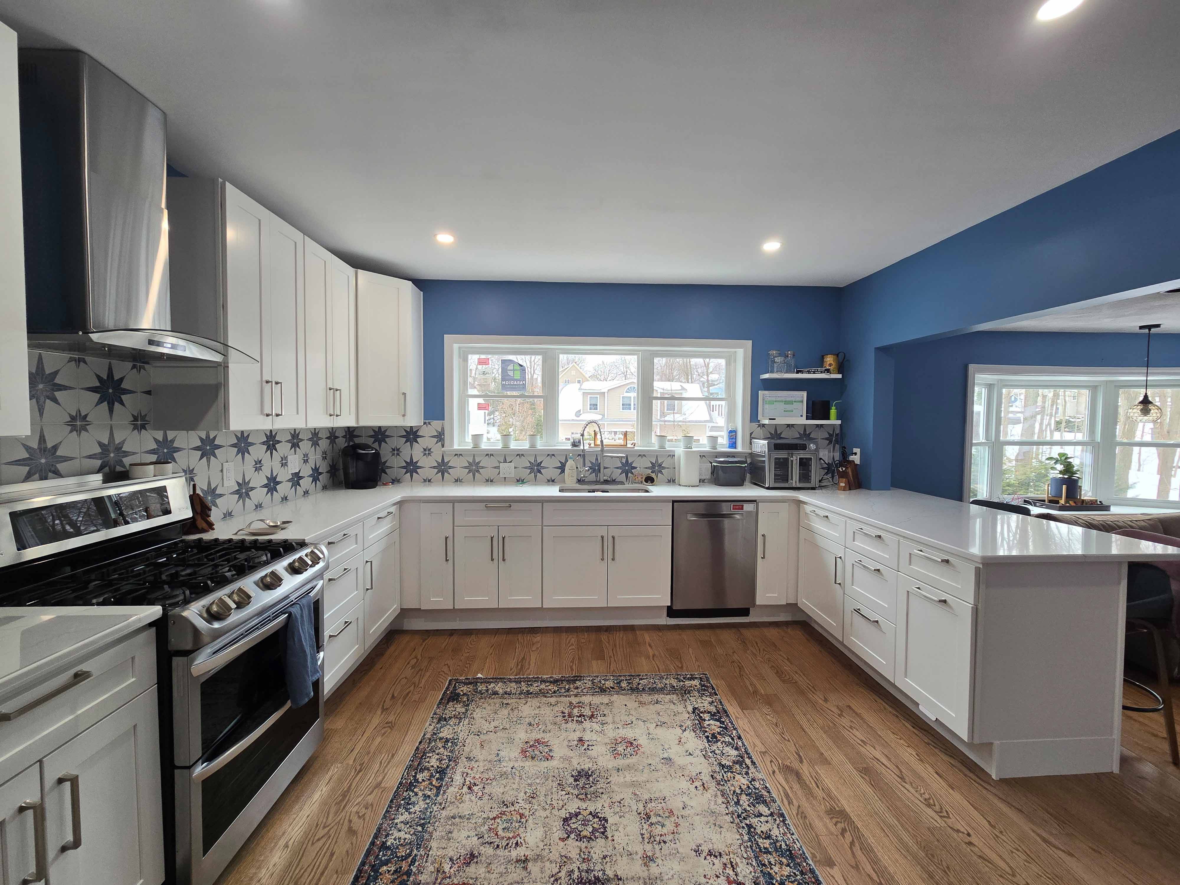Bright kitchen with white cabinets, patterned backsplash, blue walls, stainless steel appliances, and hardwood floor.