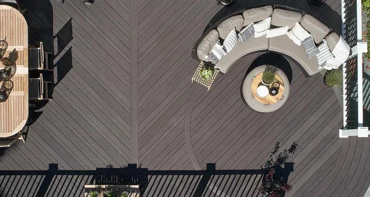 Aerial view of an outdoor deck with dark wood planks, curved sofa, and round table.