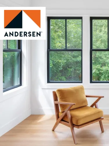 Modern orange cushioned wooden armchair near two large black-framed windows showing green trees outside.
